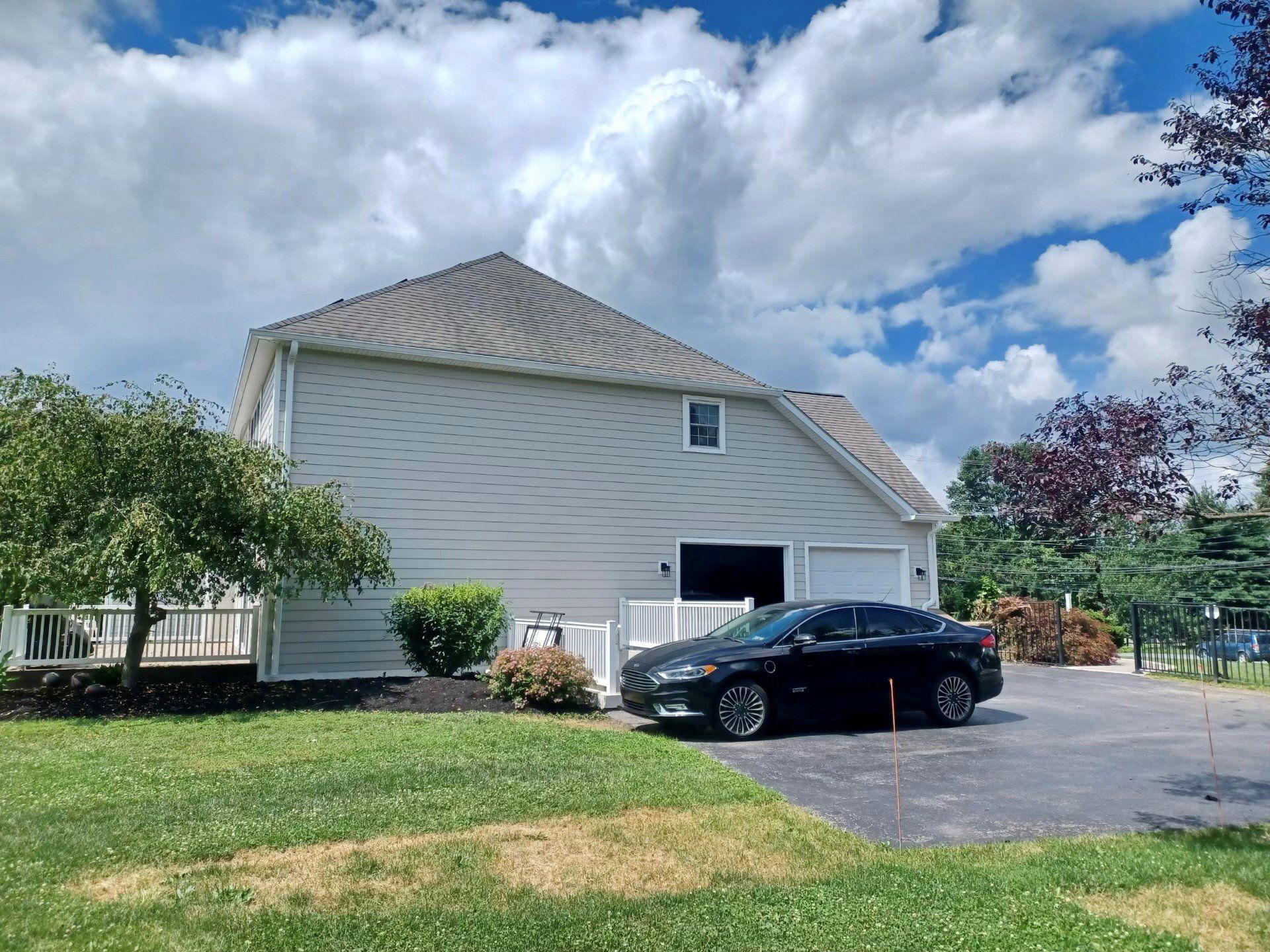 A two-story beige house with a black car parked in front on a sunny day with a cloudy sky.