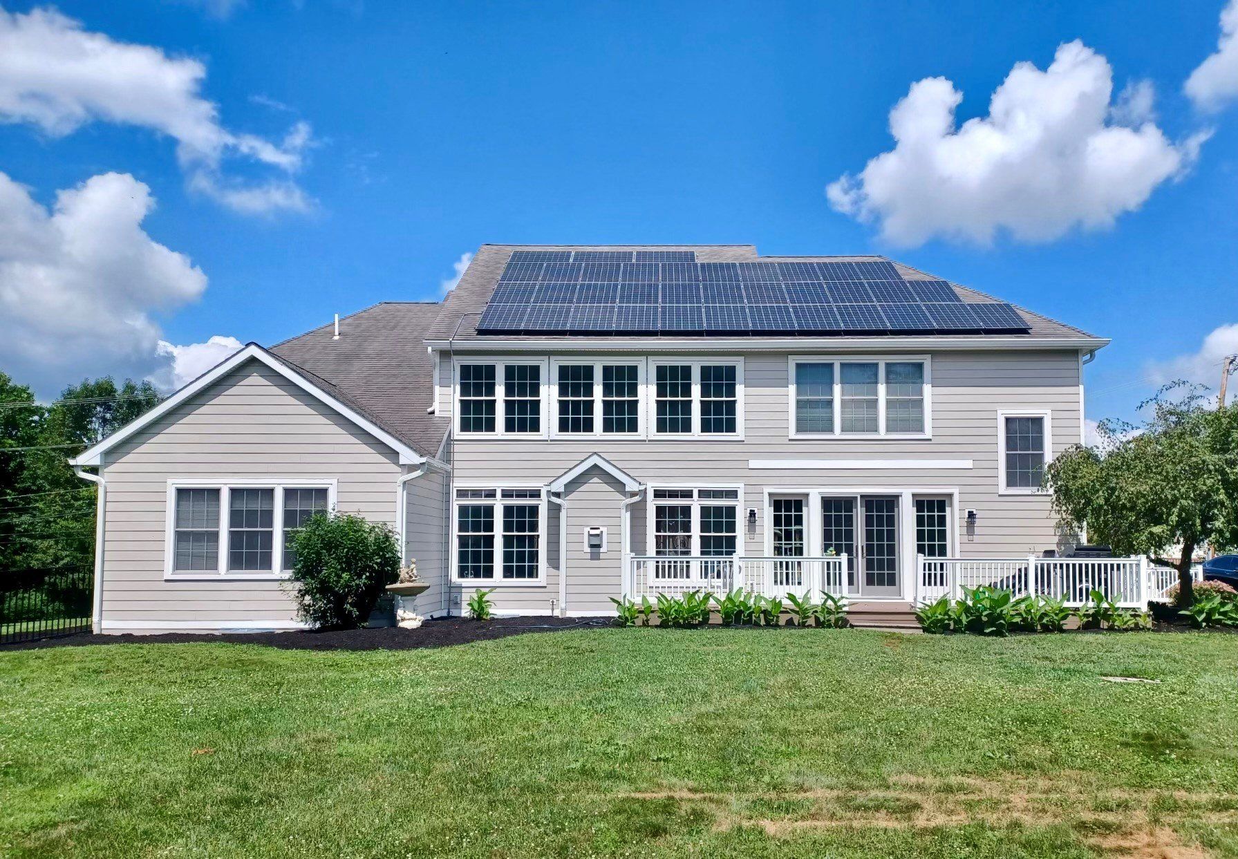 Beige house with solar panels on the roof, blue sky, and green lawn.