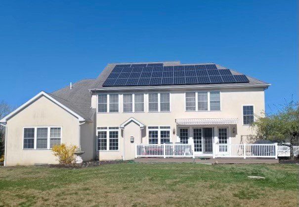 House with solar panels on the roof, white exterior, blue sky, and a backyard.