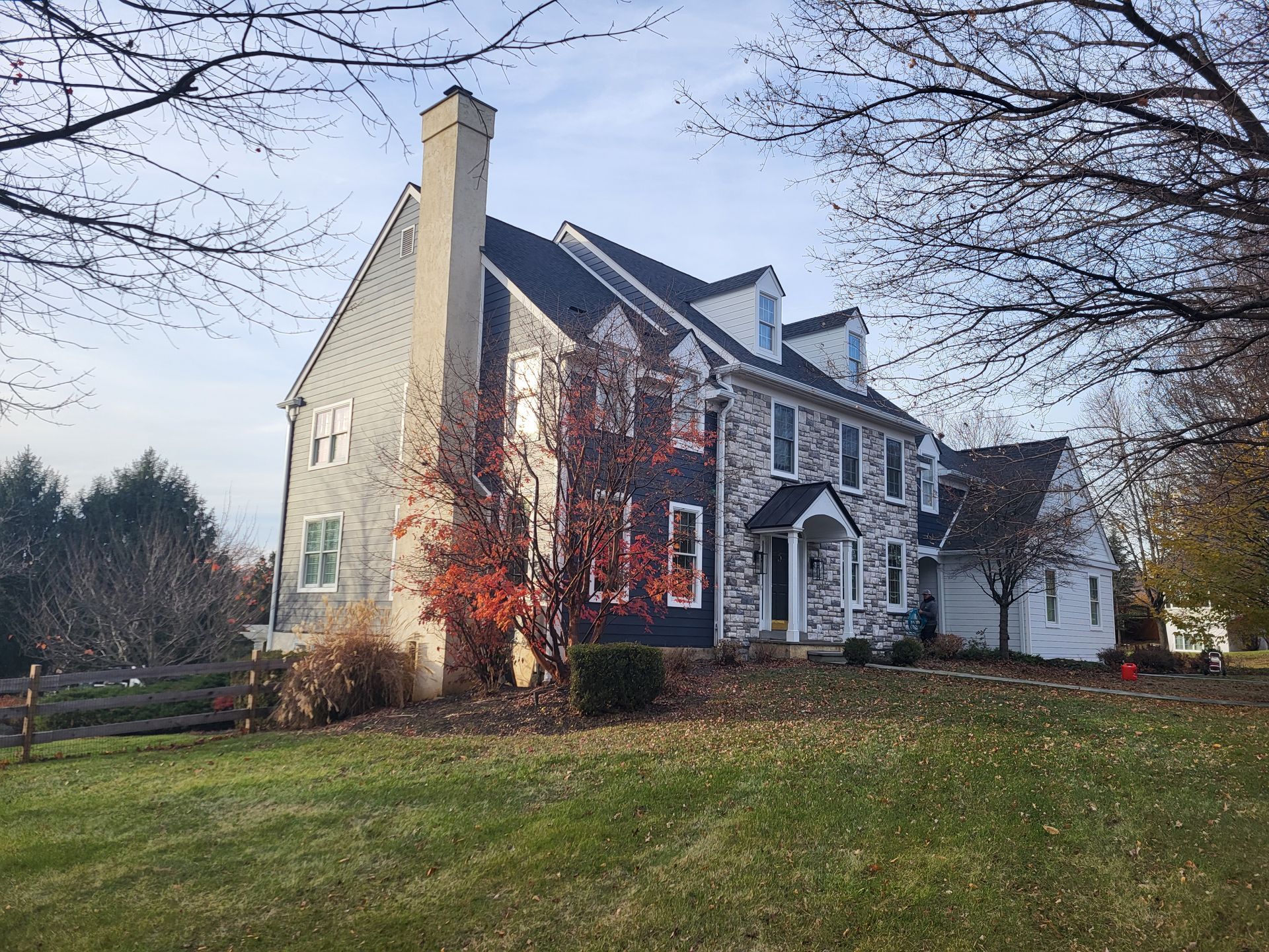 Two-story house with gray siding, stone facade, and dormer windows, set against a cloudy sky.