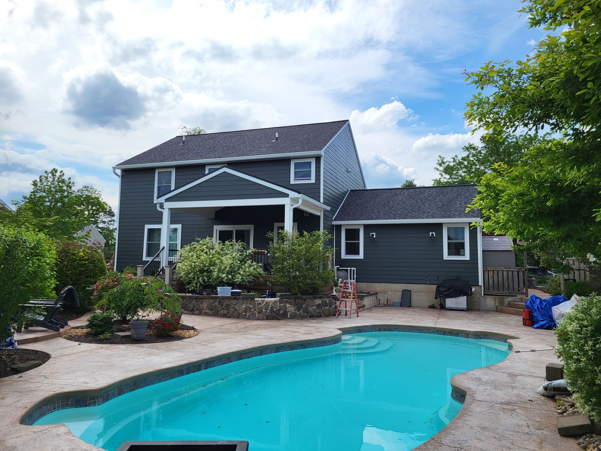A two-story house with a pool in the backyard. Blue siding and a dark roof, the pool has blue water.