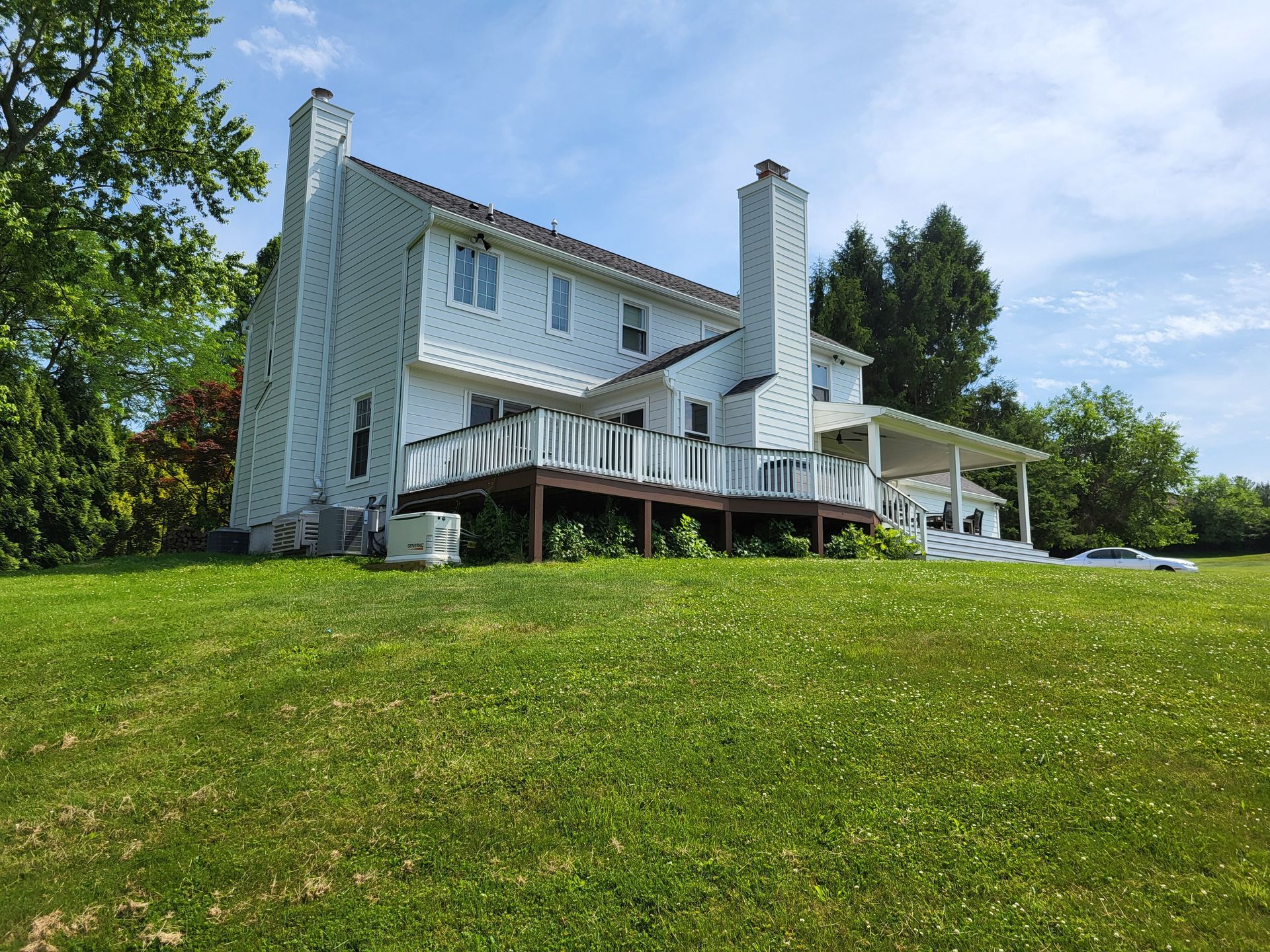 A large white house with a large deck is sitting on top of a lush green field.