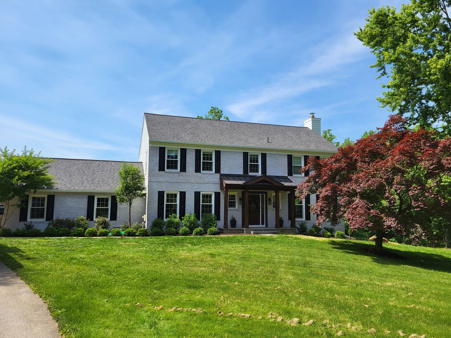 A large white house with black shutters is sitting on top of a lush green lawn.