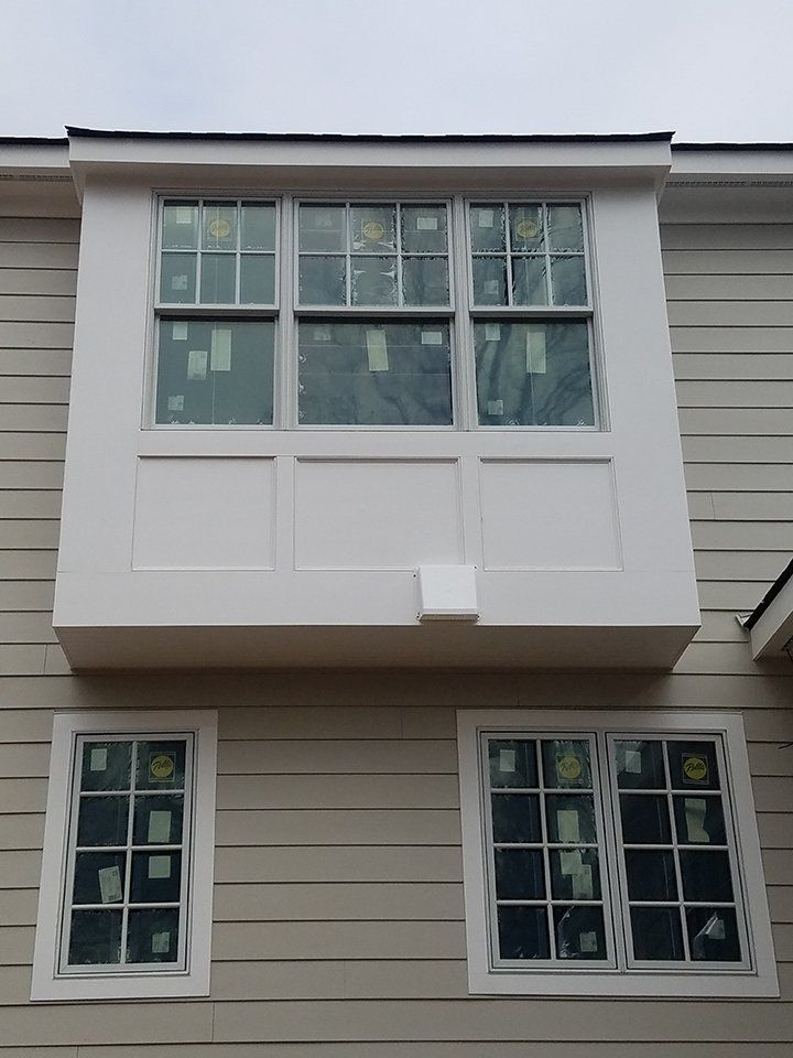 Two-story house exterior with white-framed windows, including a prominent bay window and light beige siding.