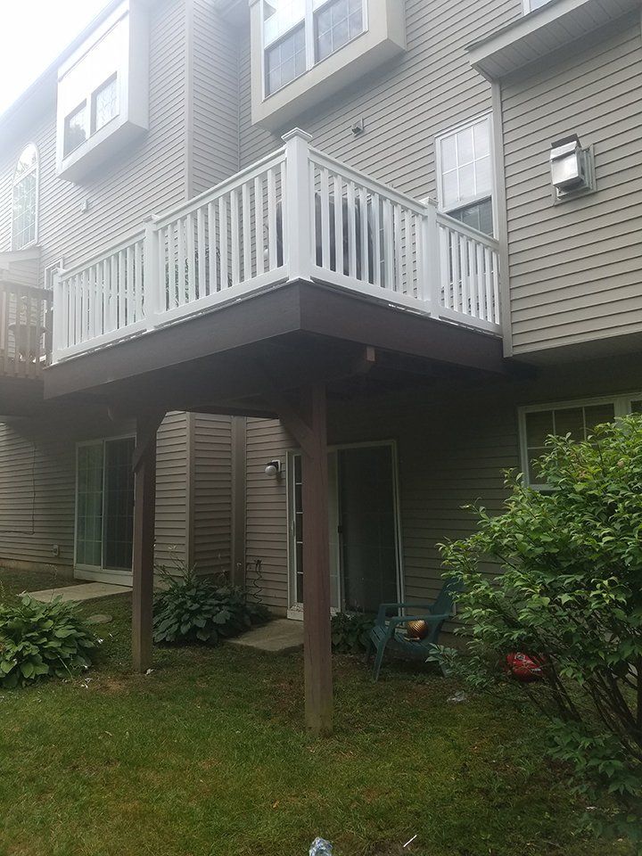 A two-story townhouse with a raised deck. Brown deck with white railing, tan siding, and green lawn.