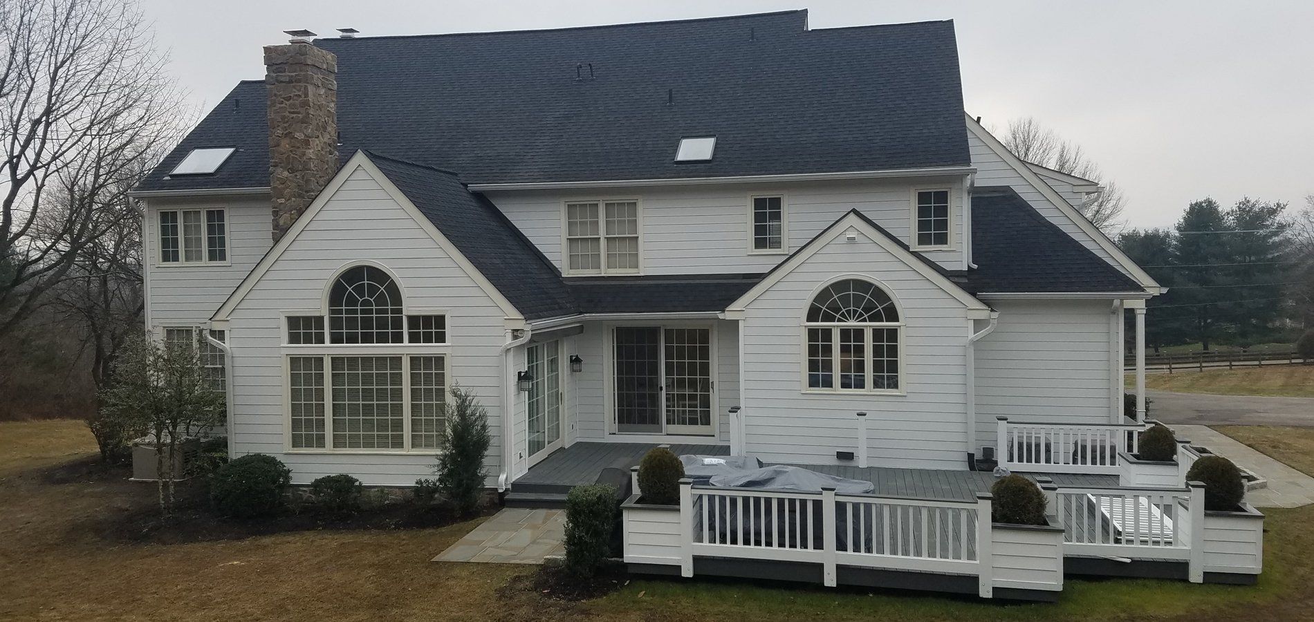 White house with a dark roof and a deck, set on a cloudy day.