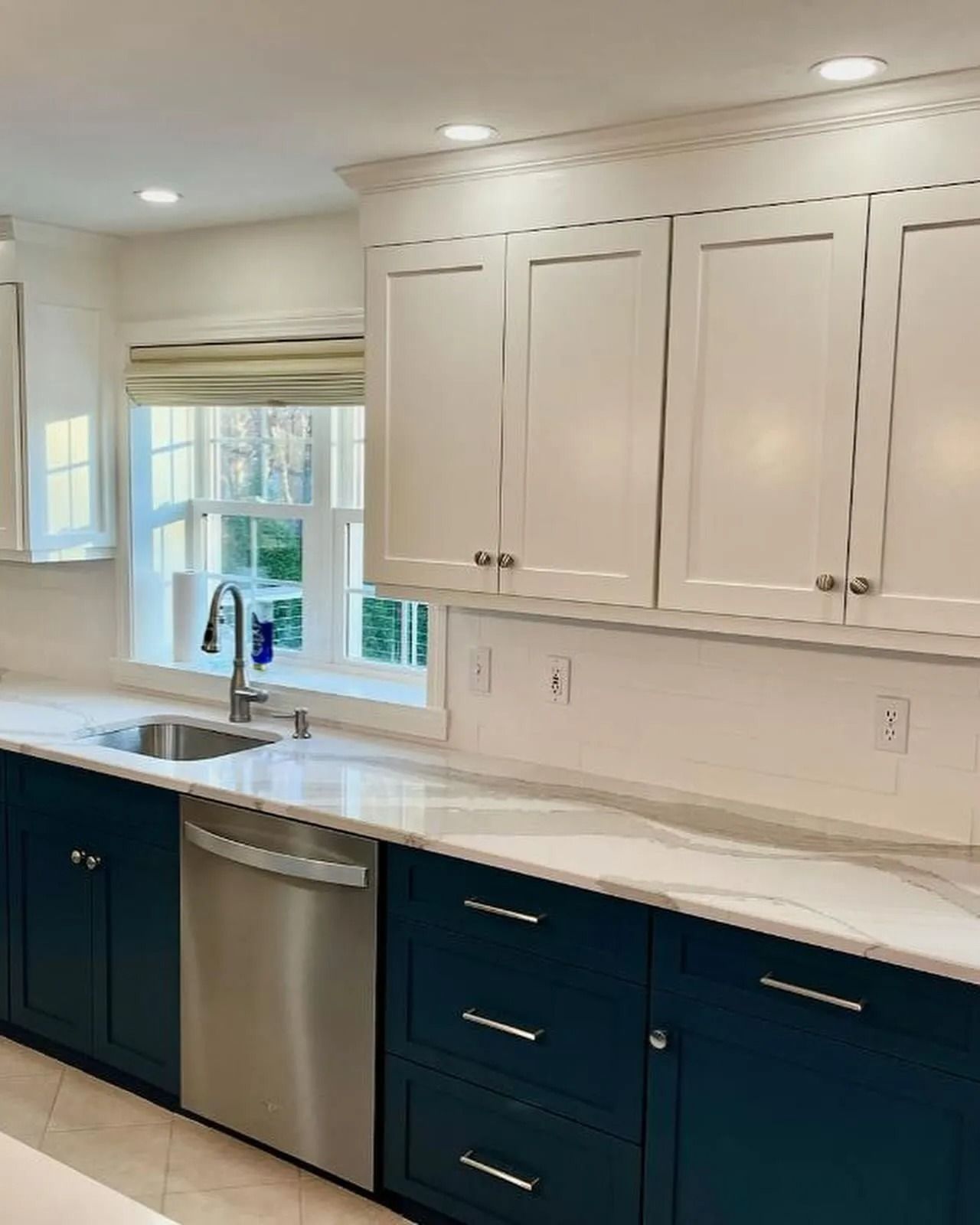 Kitchen with navy lower cabinets, white upper cabinets, stainless steel appliances, and white countertops.