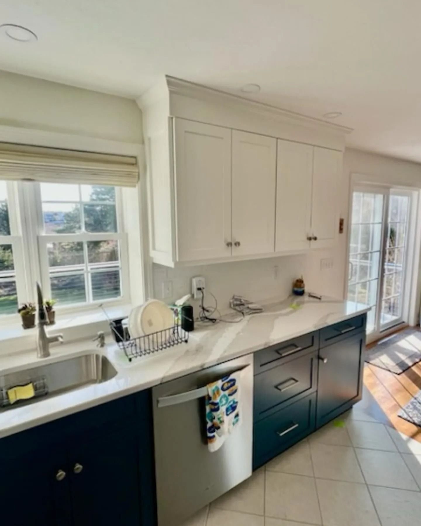 Kitchen with white upper cabinets, navy blue lower cabinets, stainless steel sink and appliances.