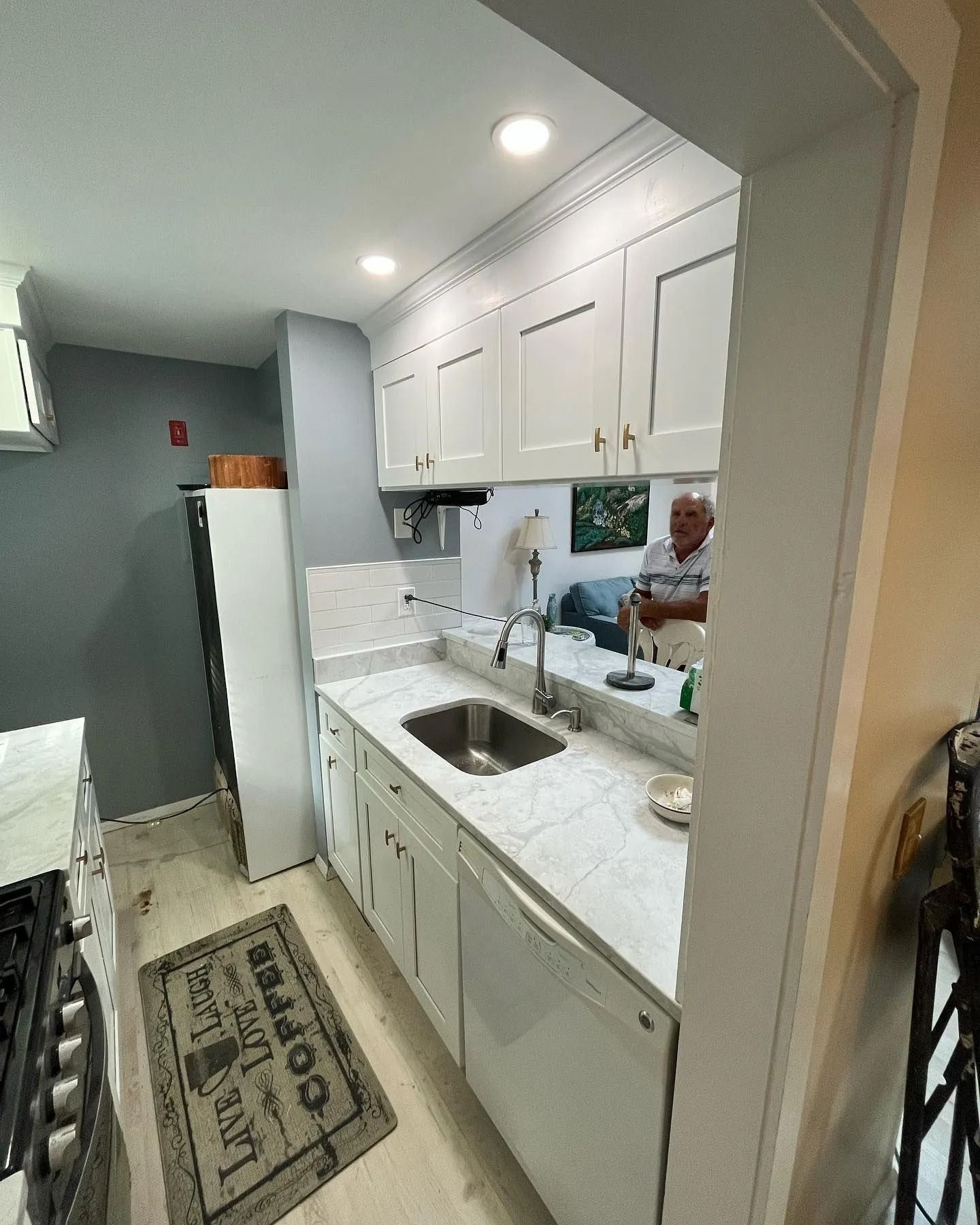 White kitchen with cabinets, sink, and appliances. A person is reflected in a mirror.