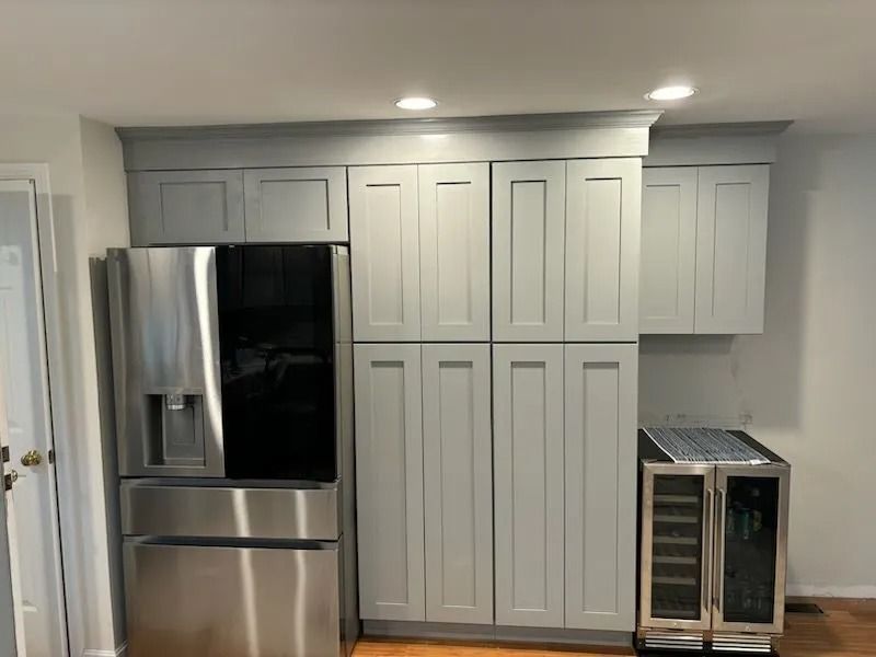 A stainless steel refrigerator and gray cabinets in a kitchen. A wine cooler is next to the cabinets.