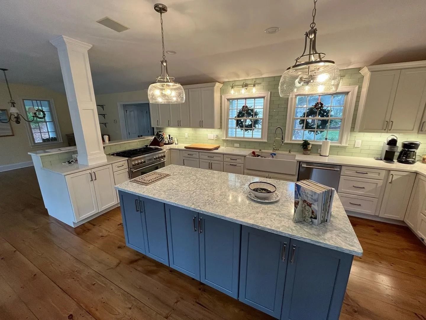 Spacious kitchen with blue island, white cabinets, and wooden floors. Two chandeliers hang over island.