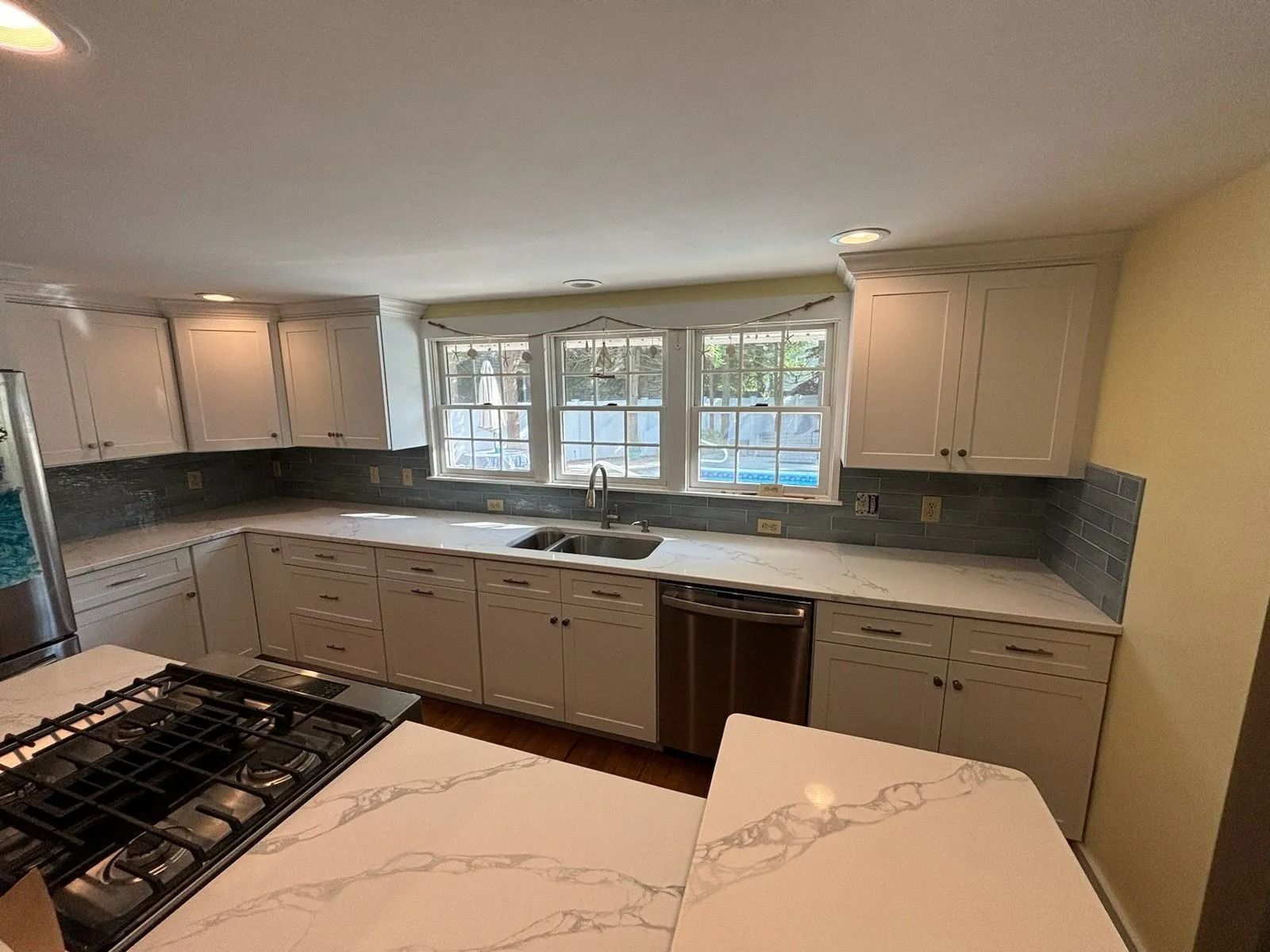 White kitchen with countertops, cabinets, windows, and an island with a gas stovetop.