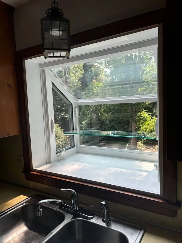 Kitchen window open to trees, above a sink. Features a glass shelf and a hanging lantern.