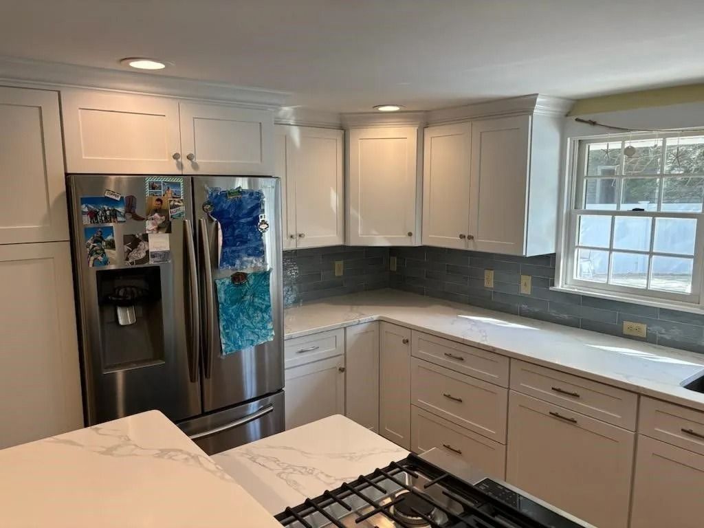 White kitchen with stainless steel refrigerator, white cabinets, and gas stovetop.