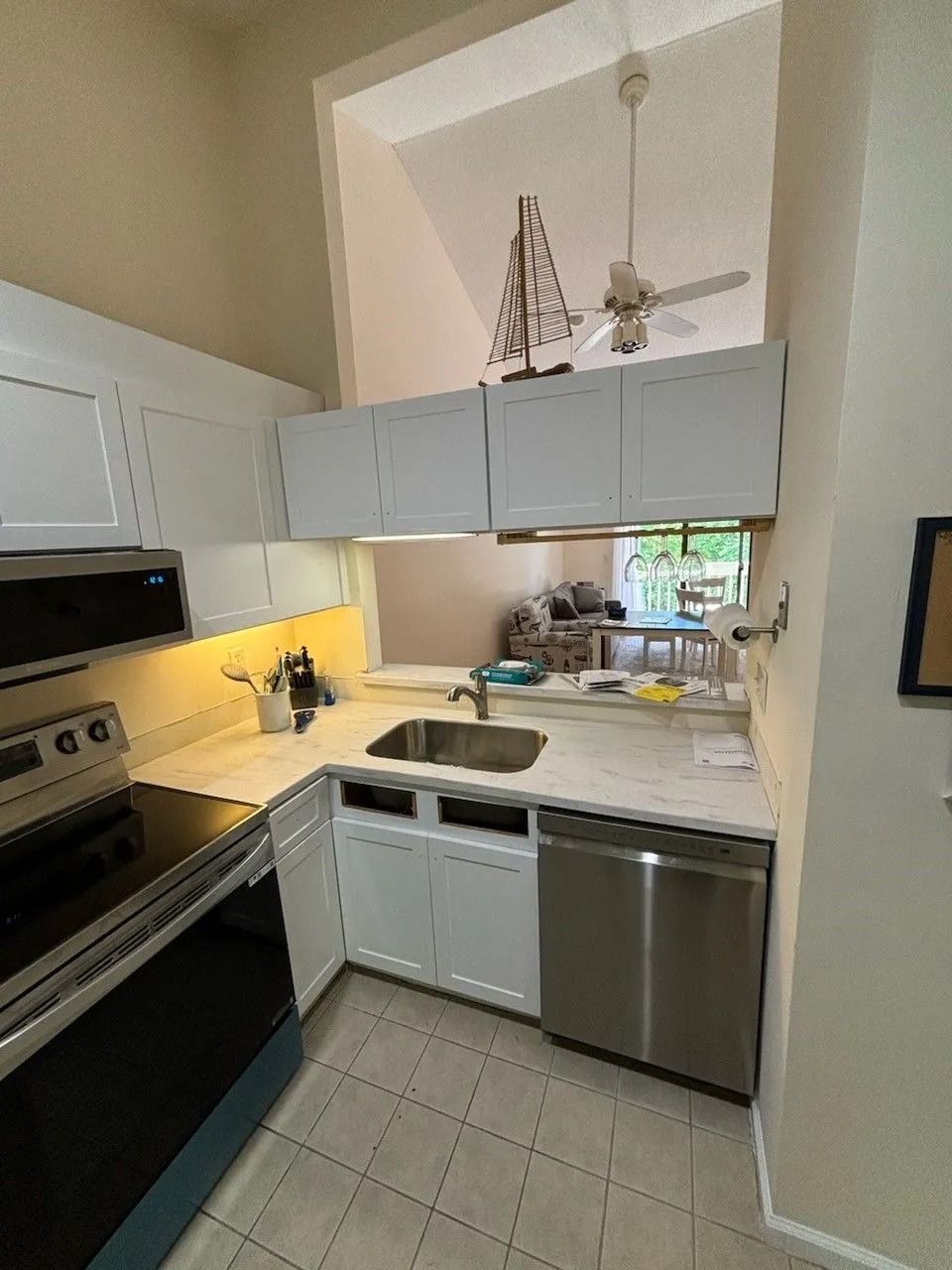 Small kitchen with white cabinets, stainless steel appliances, and a high ceiling.
