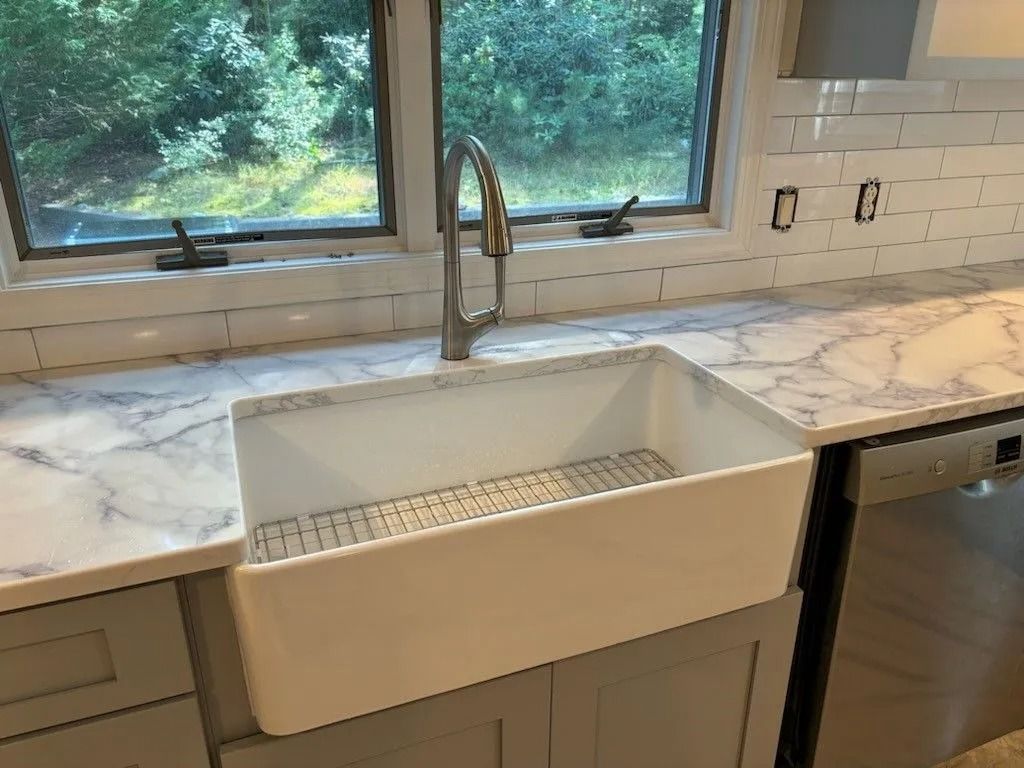Kitchen sink with marble countertop and subway tile backsplash. Gray cabinets, stainless faucet, and a window in the background.