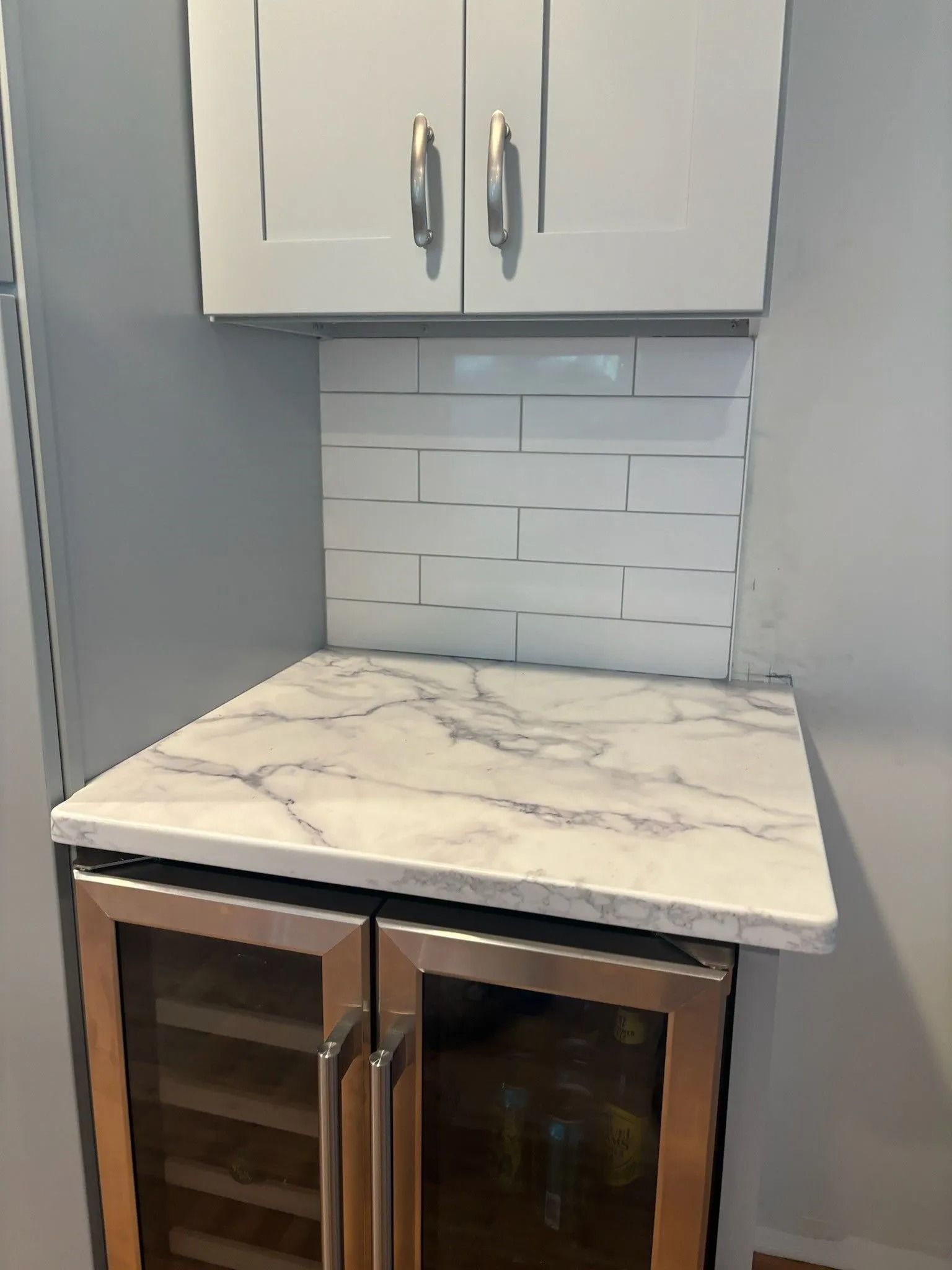 Bar area with wine fridge, countertop, white subway tile backsplash, and upper cabinets.
