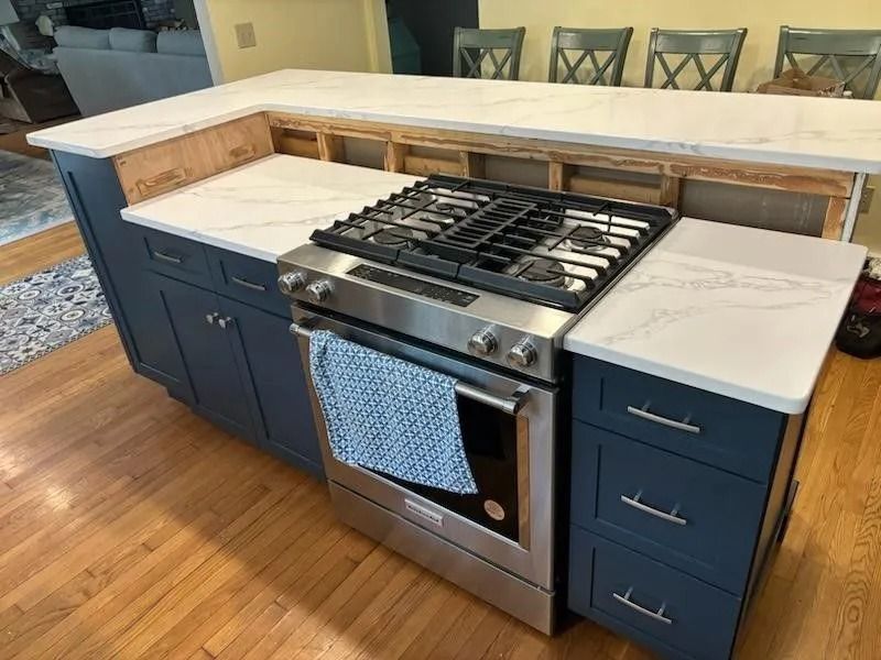 Kitchen island with a stove, dark blue cabinets, and white countertops.
