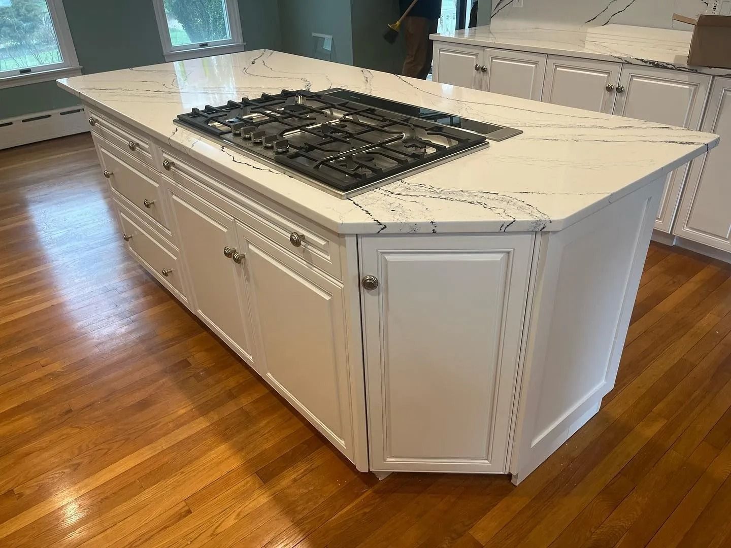 Kitchen island with gas stovetop, white cabinets, and marble countertop on a hardwood floor.