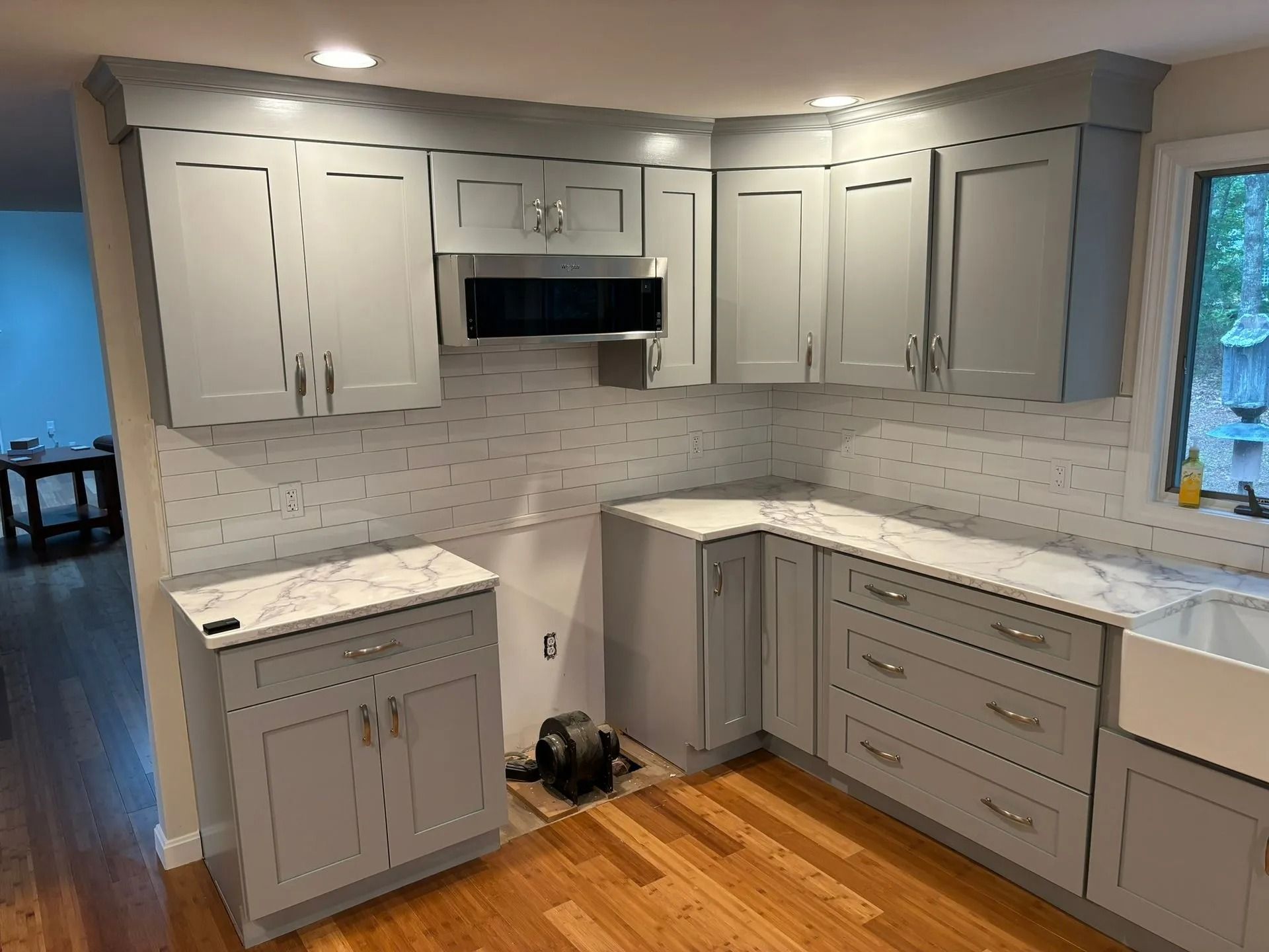 Gray kitchen cabinets with white countertops and backsplash. Wooden floor.