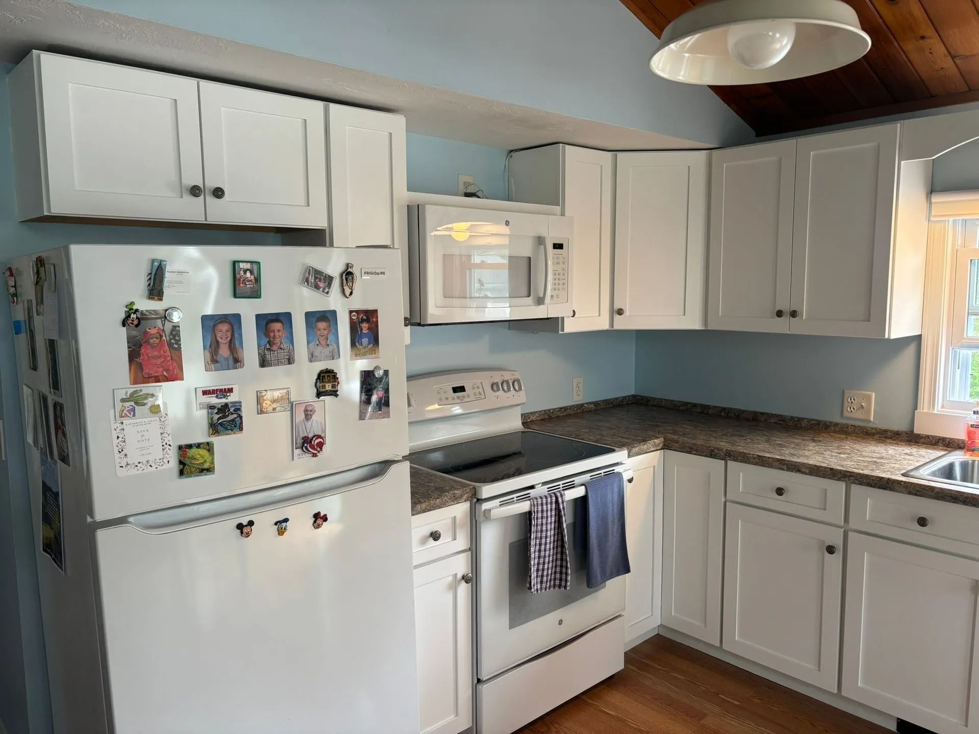 White kitchen with white cabinets, appliances, and a microwave above the stove, blue walls.
