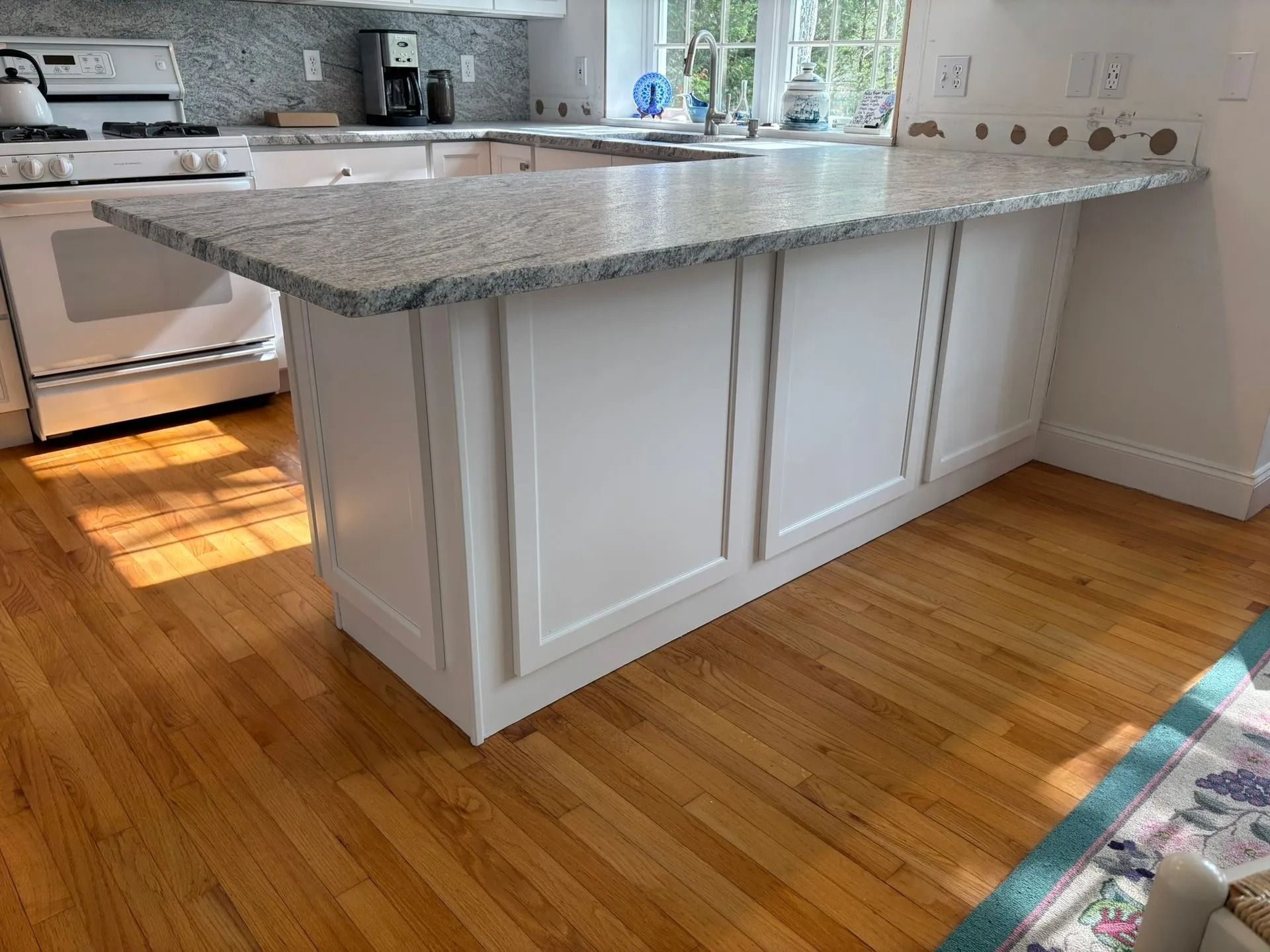White kitchen island with granite countertop, set in a room with hardwood floors and bright sunlight.