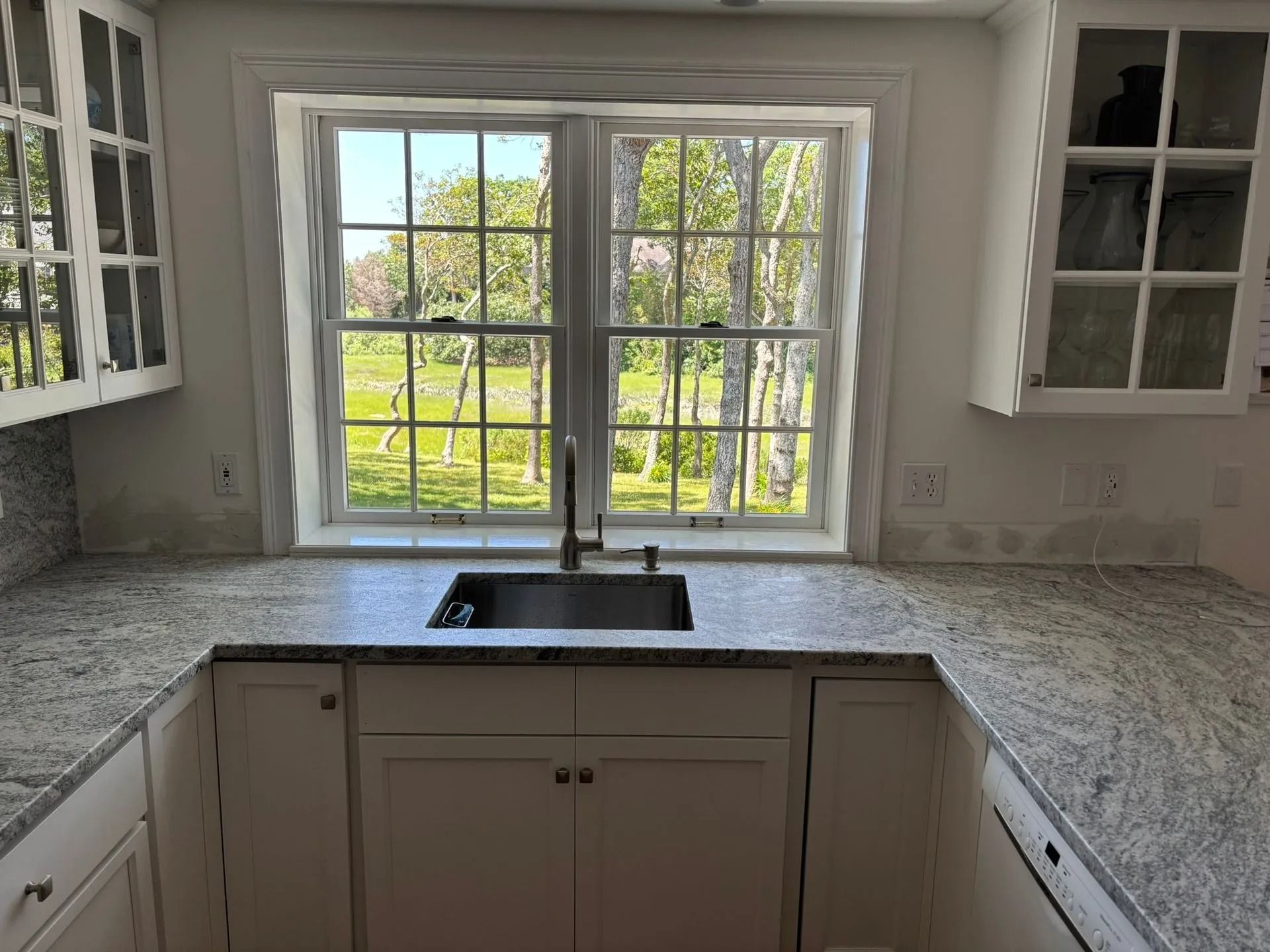 Kitchen with granite countertop, sink under a window, and white cabinets.