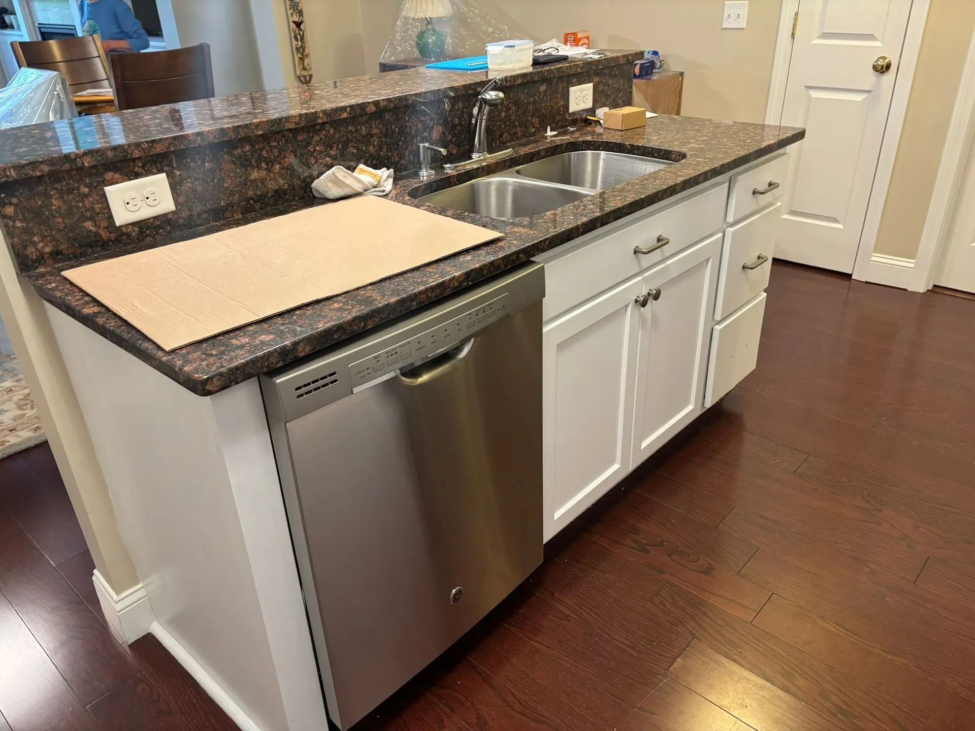 Kitchen island with stainless steel dishwasher and sink, white cabinets, and brown countertop.
