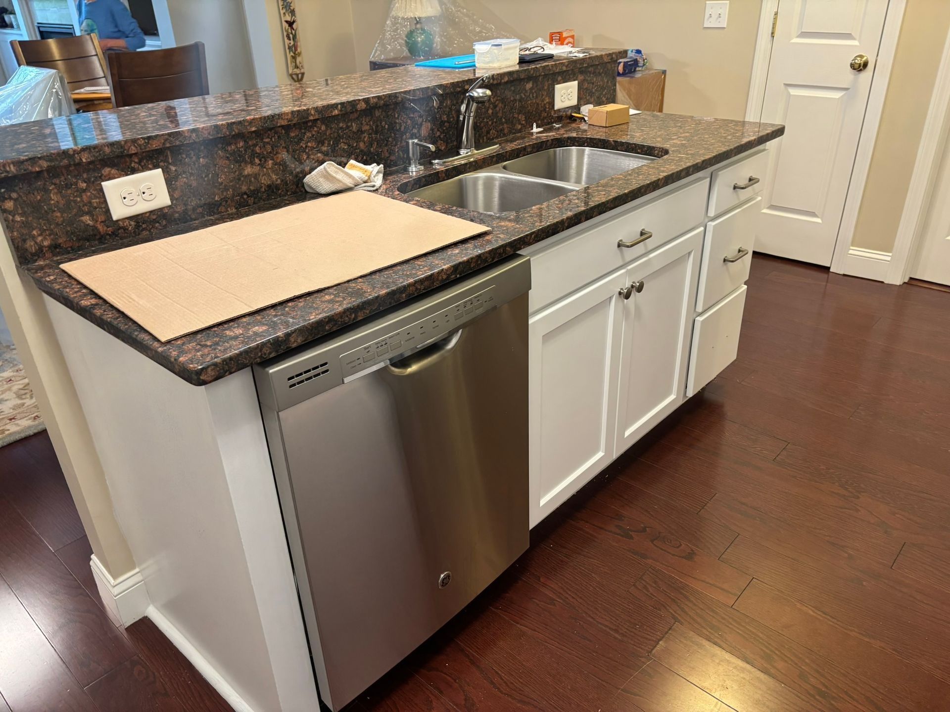 Kitchen island with stainless steel dishwasher and sink, white cabinets, and brown granite countertop.