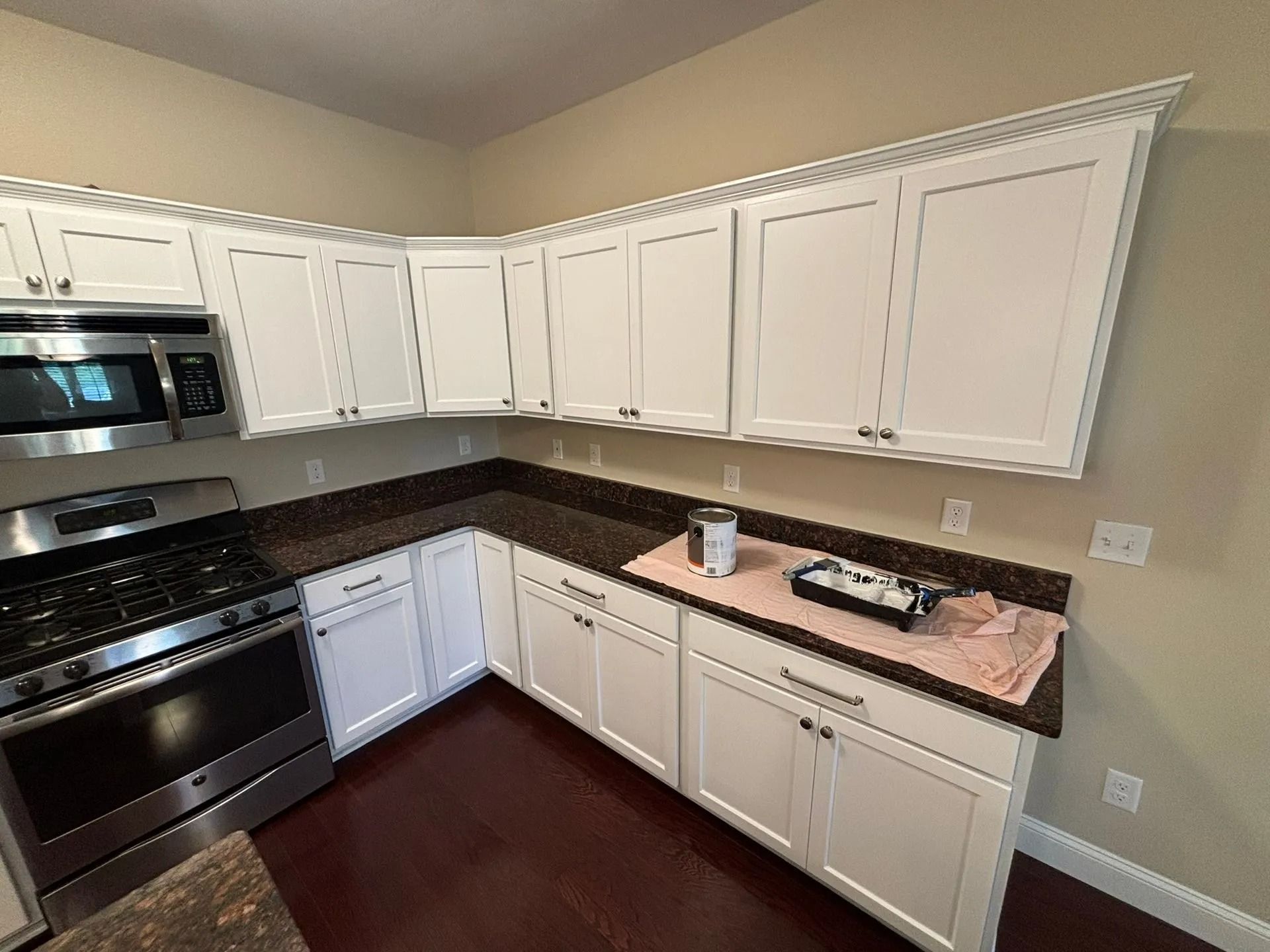 White kitchen cabinets, brown countertop, and stainless steel appliances. Painting supplies on counter.