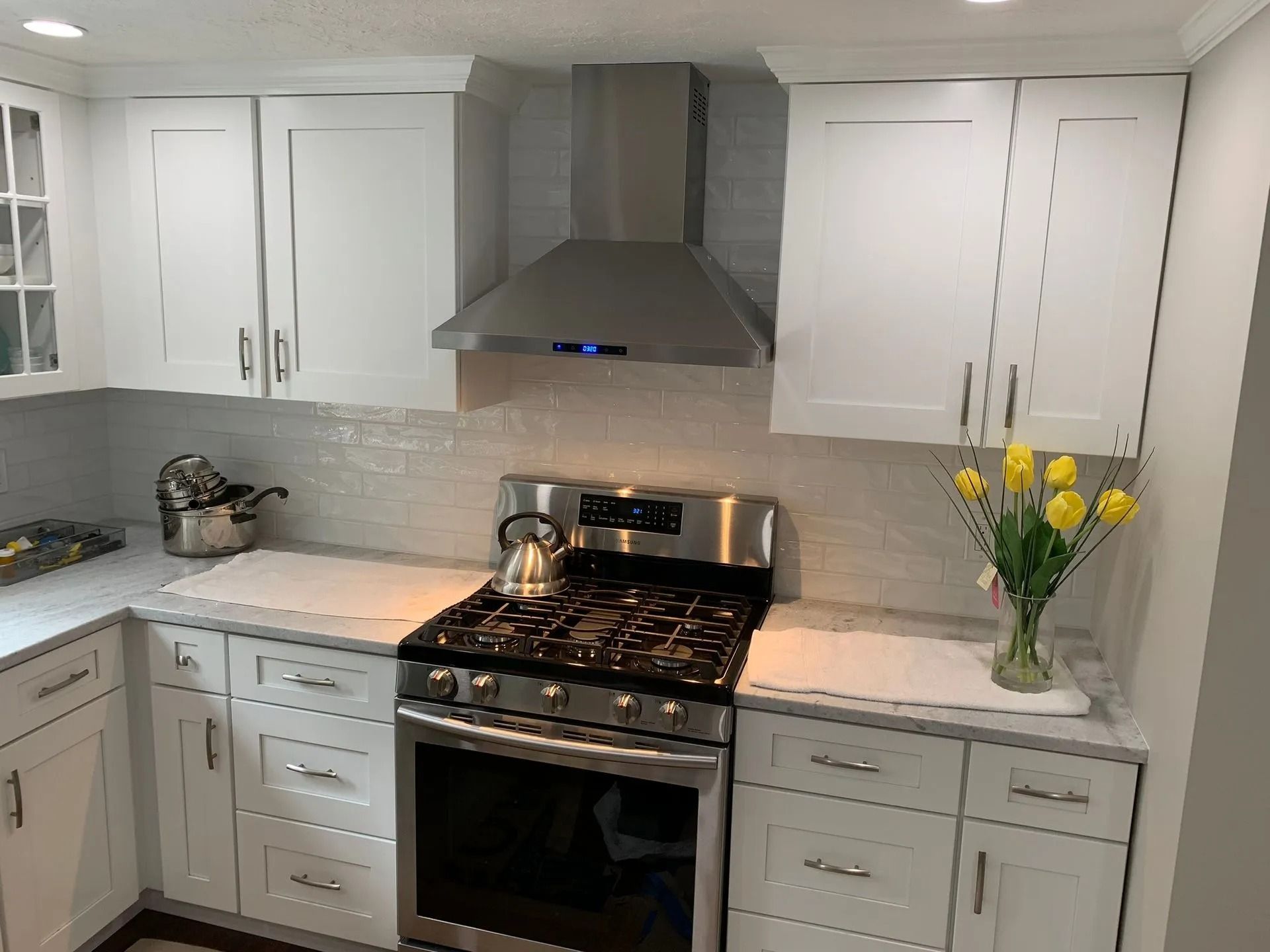 White kitchen with stainless steel appliances. Range hood over stove, white cabinets, light countertops.