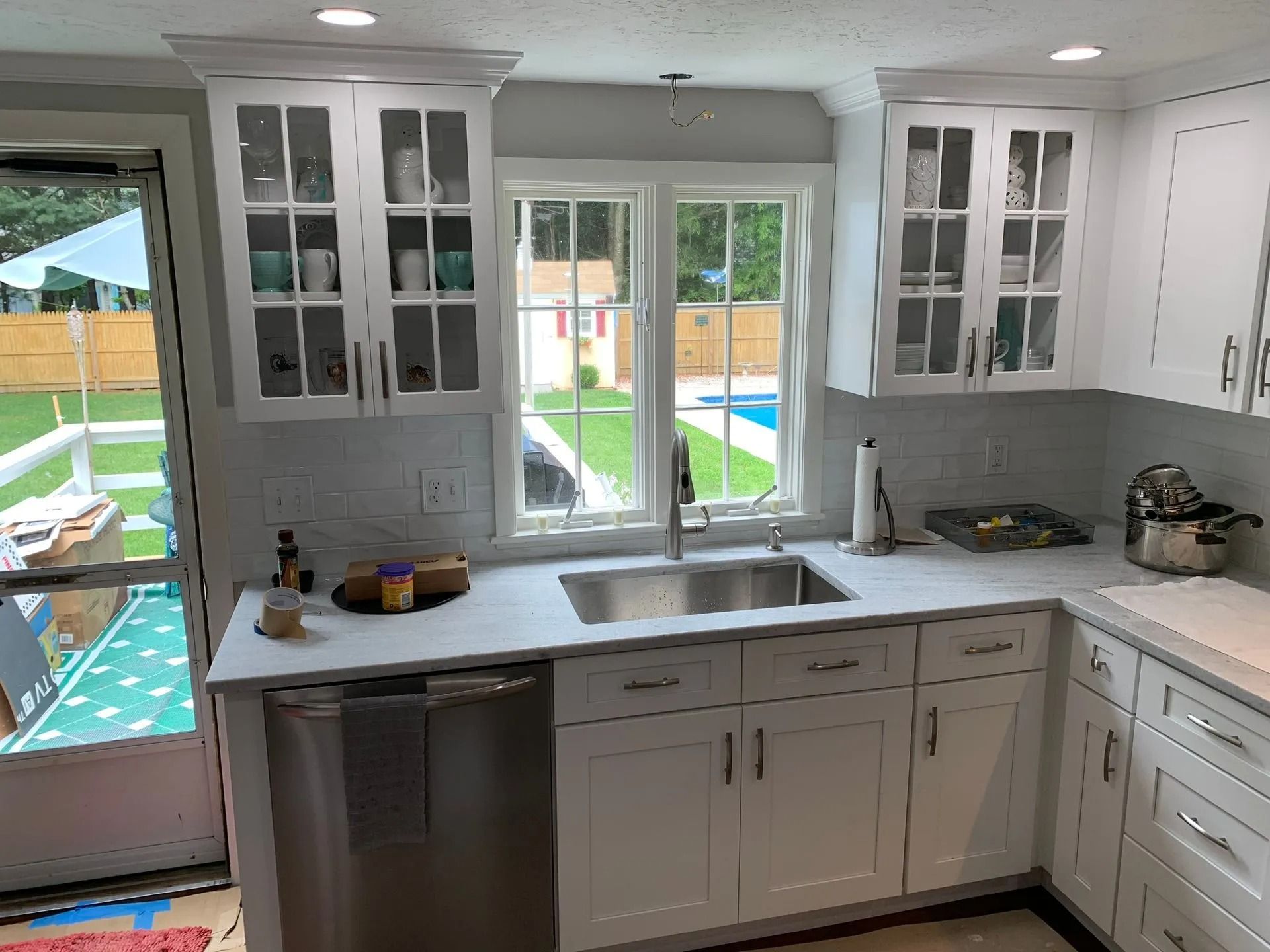 White kitchen with countertops, cabinets, and a sink. A window overlooks a backyard with a pool.