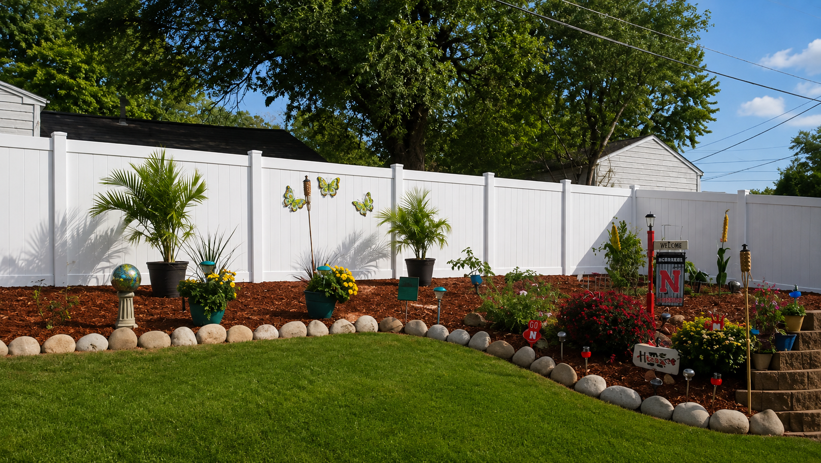 White vinyl fence in a backyard garden with lawn and potted plants.
