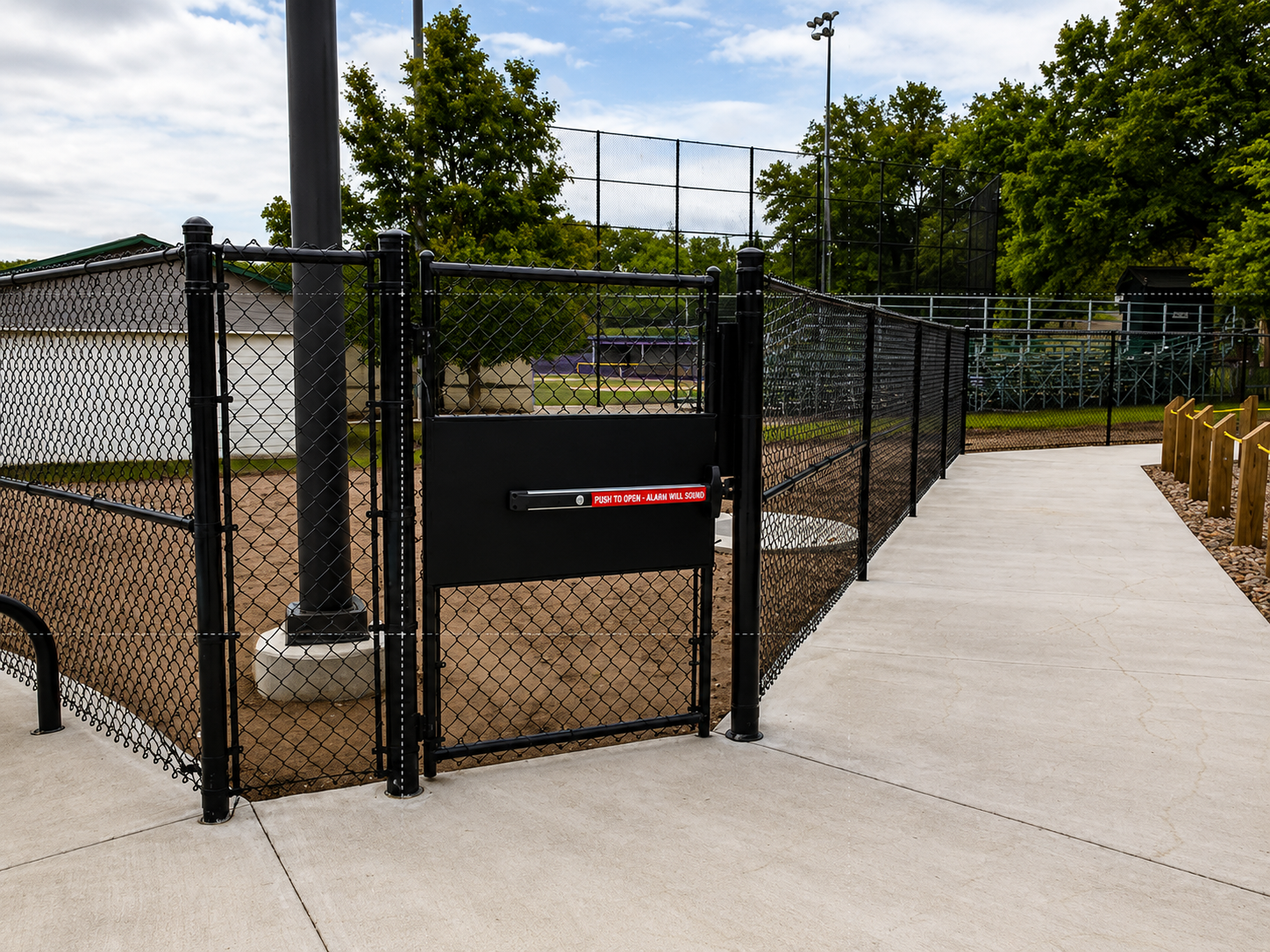 Black chain-link fence with a gate, leading to a concrete path. A sign reads 