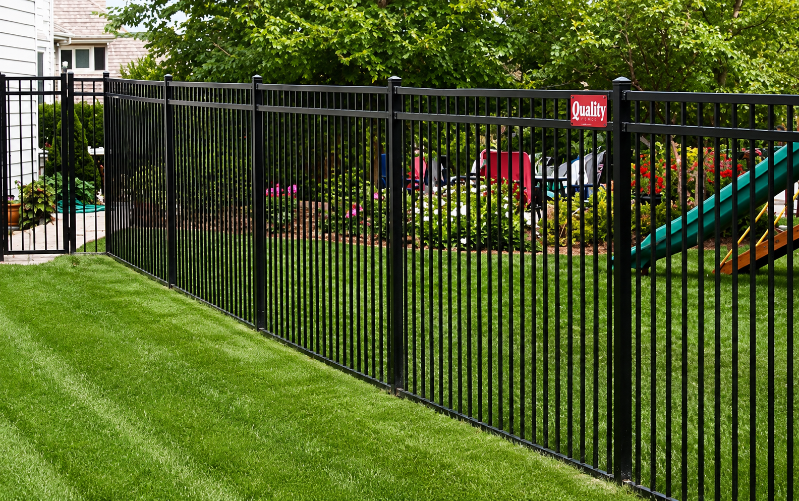 Black metal fence encloses a green lawn, with a slide visible behind it.