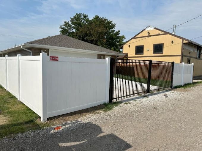 White vinyl fence enclosing a gravel area, with a black metal gate. A yellow building is visible.