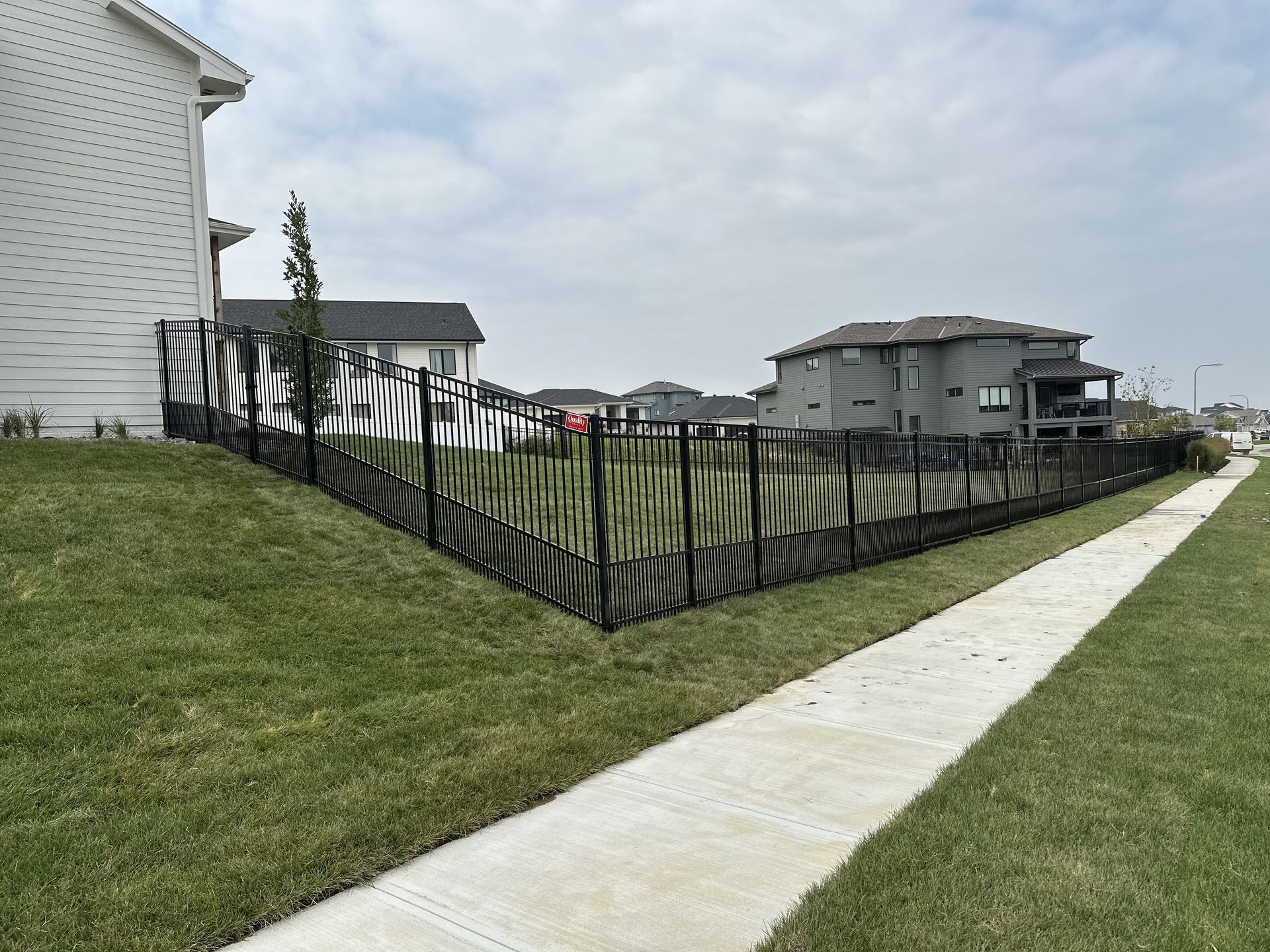 Black fence with a striped design surrounds a grassy lot next to a sidewalk.