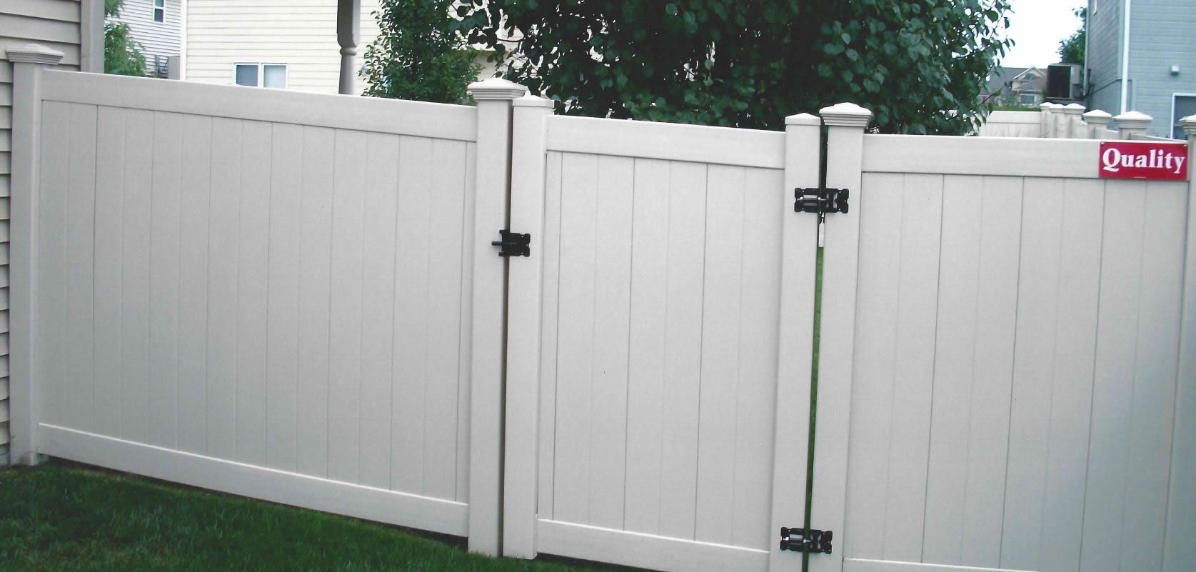White vinyl fence with gate, set in a grassy yard, with a building in the background.