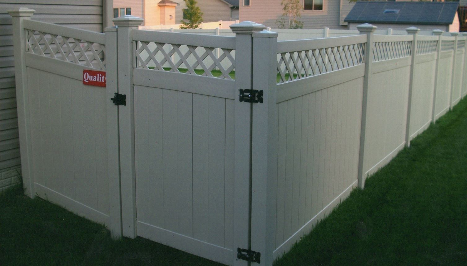 Beige vinyl fence with a matching gate, surrounding a grassy yard.