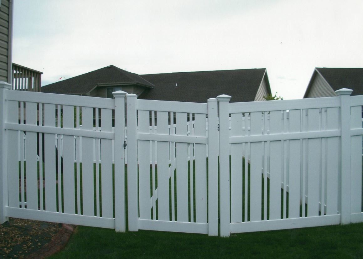 White vinyl fence in a yard, partially surrounding a house with dark roof.