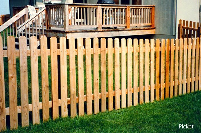 Wooden picket fence in front of a raised wooden deck and green lawn.