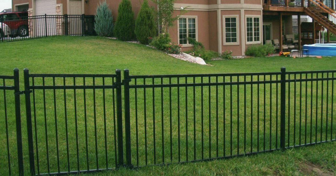 Black metal fence enclosing a green lawn in front of a light brown house.