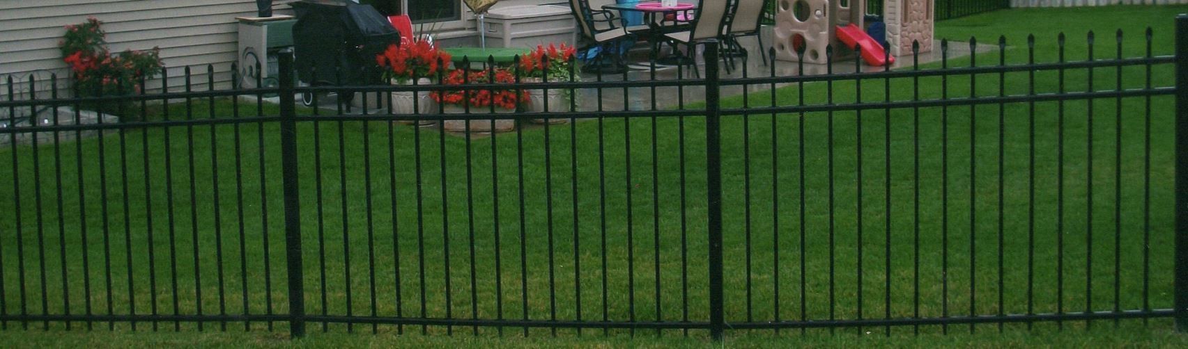 Black metal fence surrounding a grassy yard with a playground in the background.