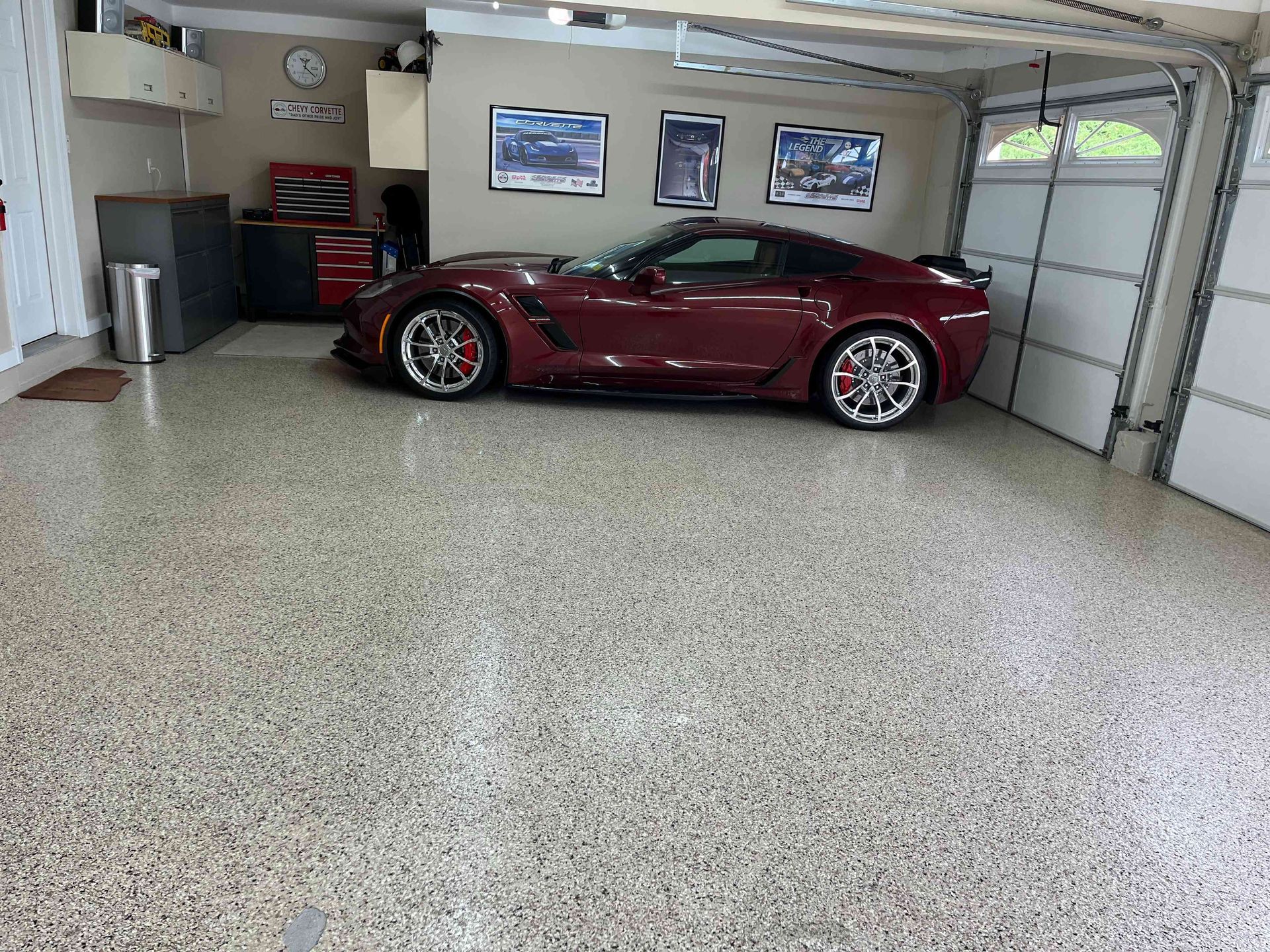 Burgundy sports car in a garage with epoxy flooring and decorative storage.