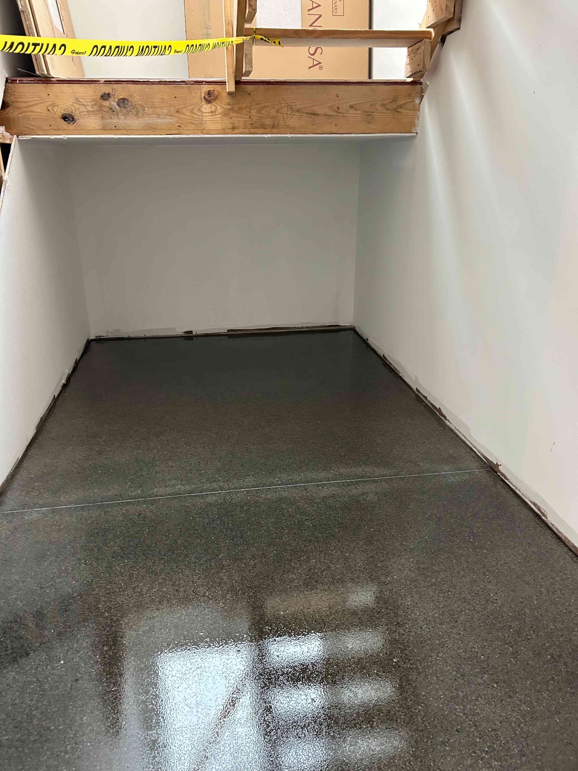 A small, gray-floored room with white walls under a wooden beam. Construction tape is visible.