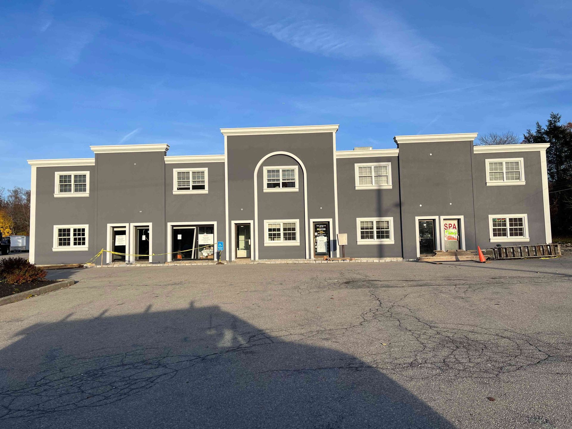 Gray commercial building with white trim under a blue sky, empty gravel lot.