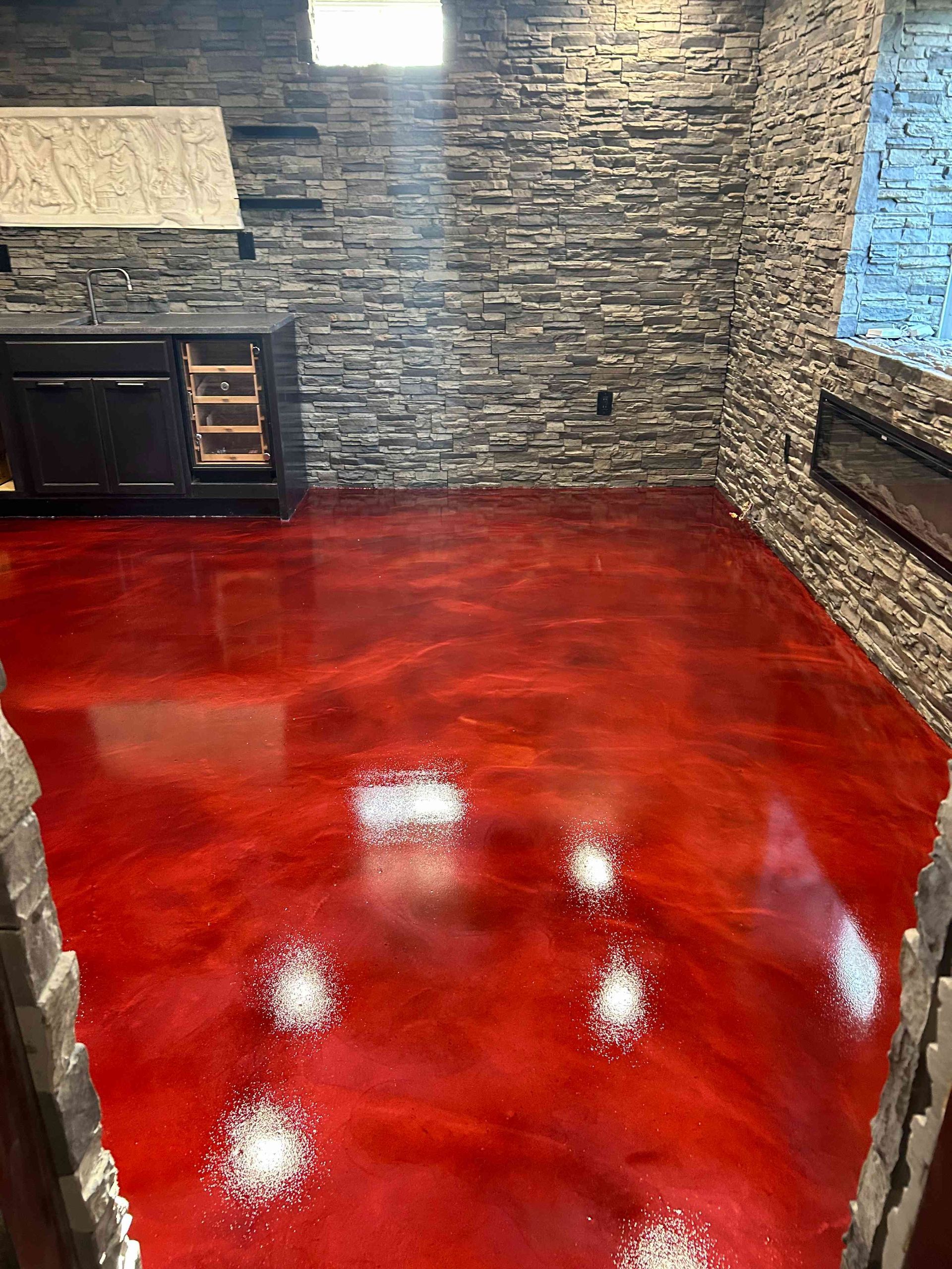 Red metallic epoxy floor in a room with a stone accent wall and black cabinetry.