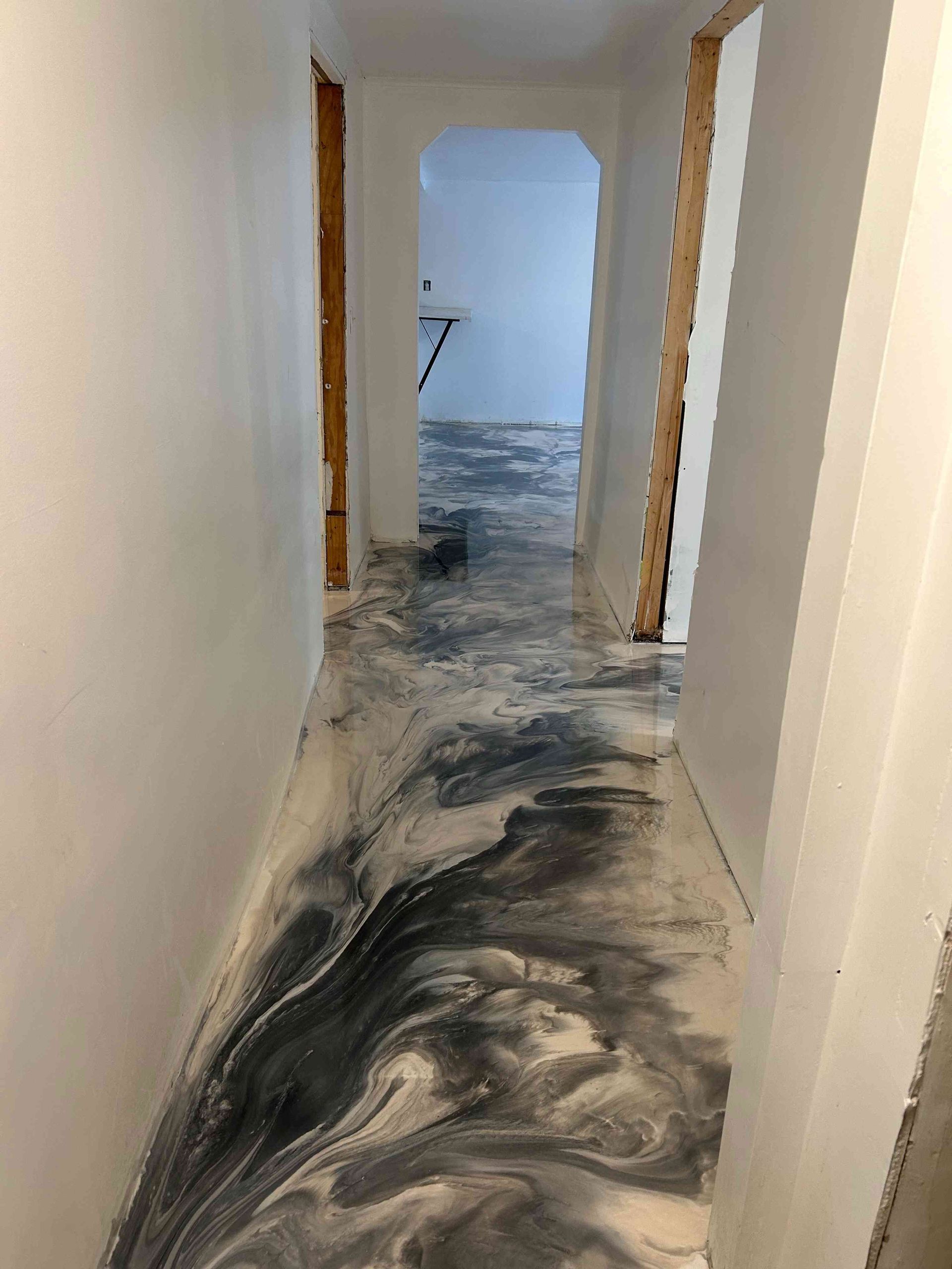 Hallway with epoxy floor, black and white swirls. White walls, doorway, wood framing visible.