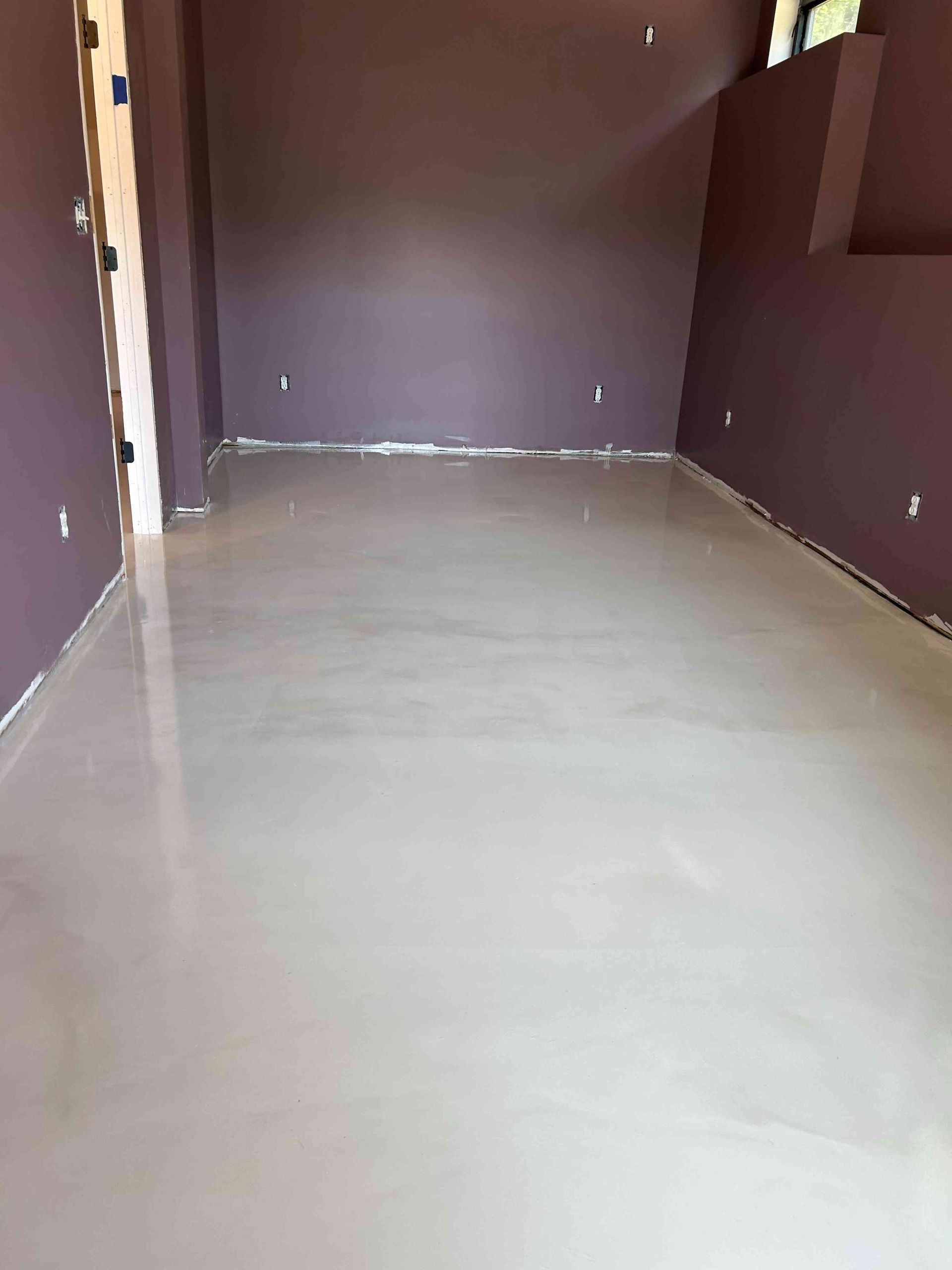 Room with freshly poured light gray concrete floor and plum colored walls.