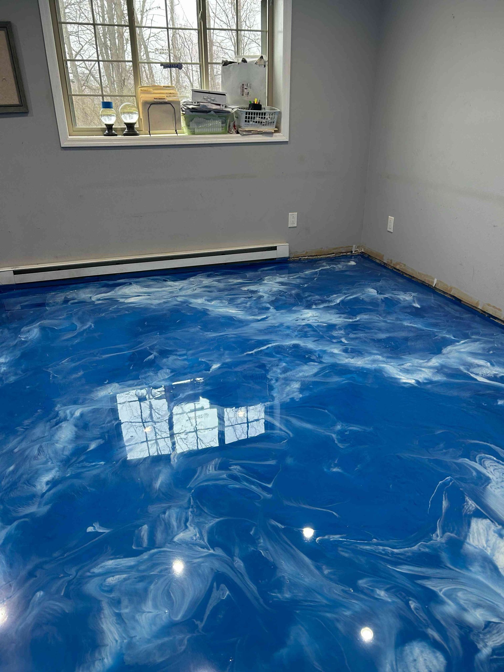 Blue epoxy flooring with white swirling patterns in a room with gray walls and a window.